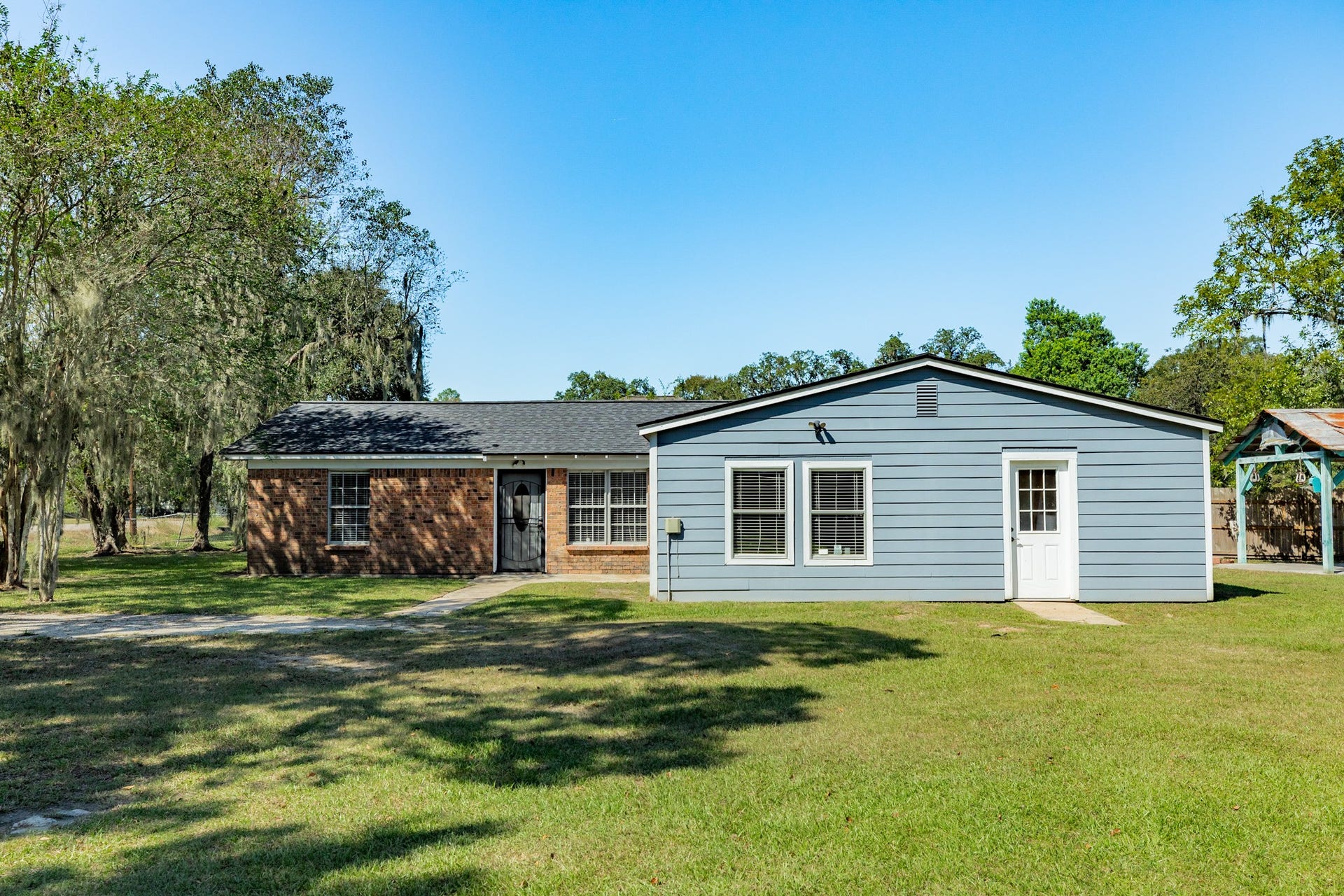 1602 County Road 939, Sweeny, TX 77480 Spacious single-story home offers a distinctive combination of brick and blue-gray siding, with multiple windows welcoming natural light. An expansive grassy lawn provides plenty of room for outdoor activities.