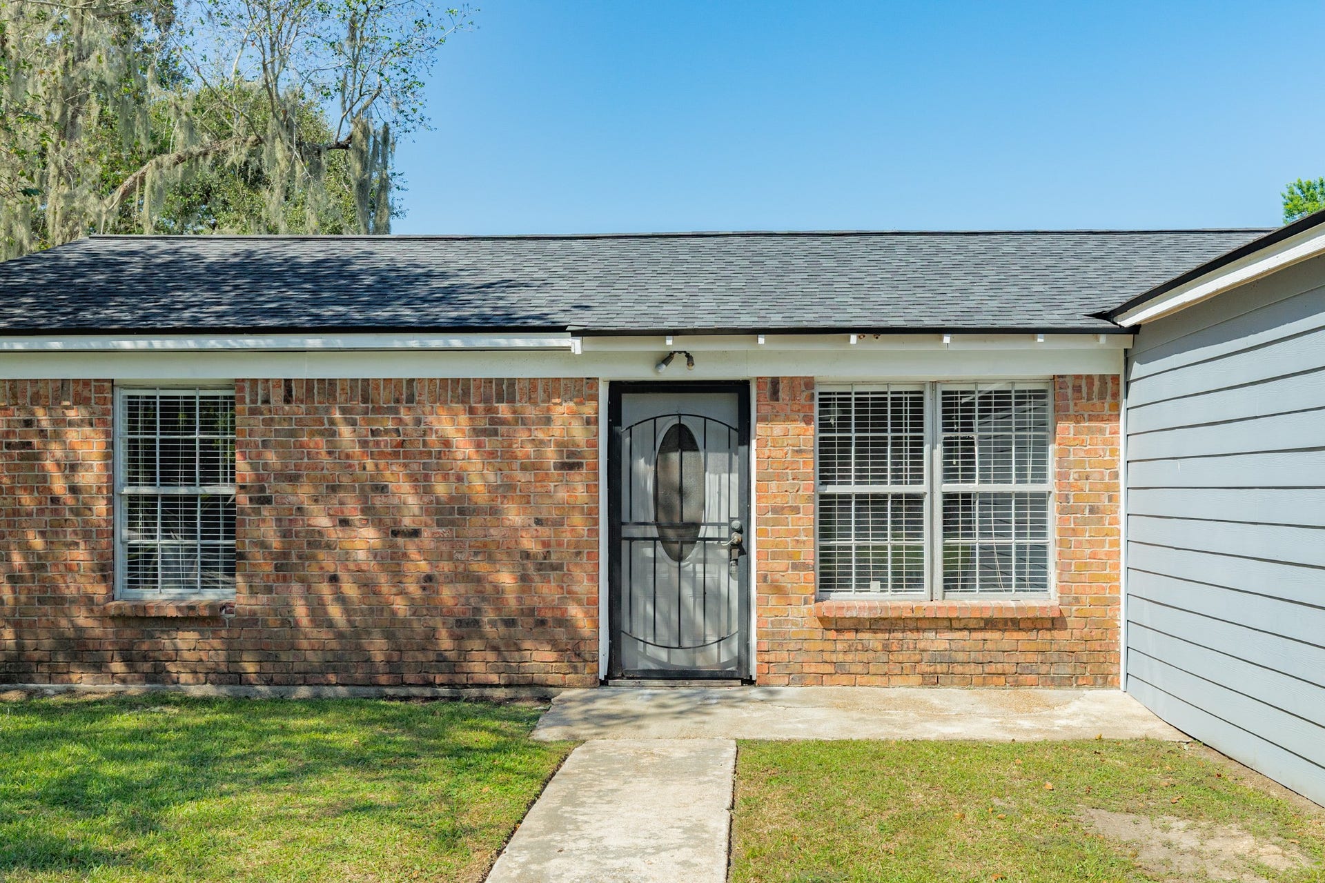 1602 County Road 939, Sweeny, TX 77480 Charming brick faade features a decorative security door, white-trimmed windows, and a concrete walkway. Natural brick tones and mature landscaping add character to the home's entrance.