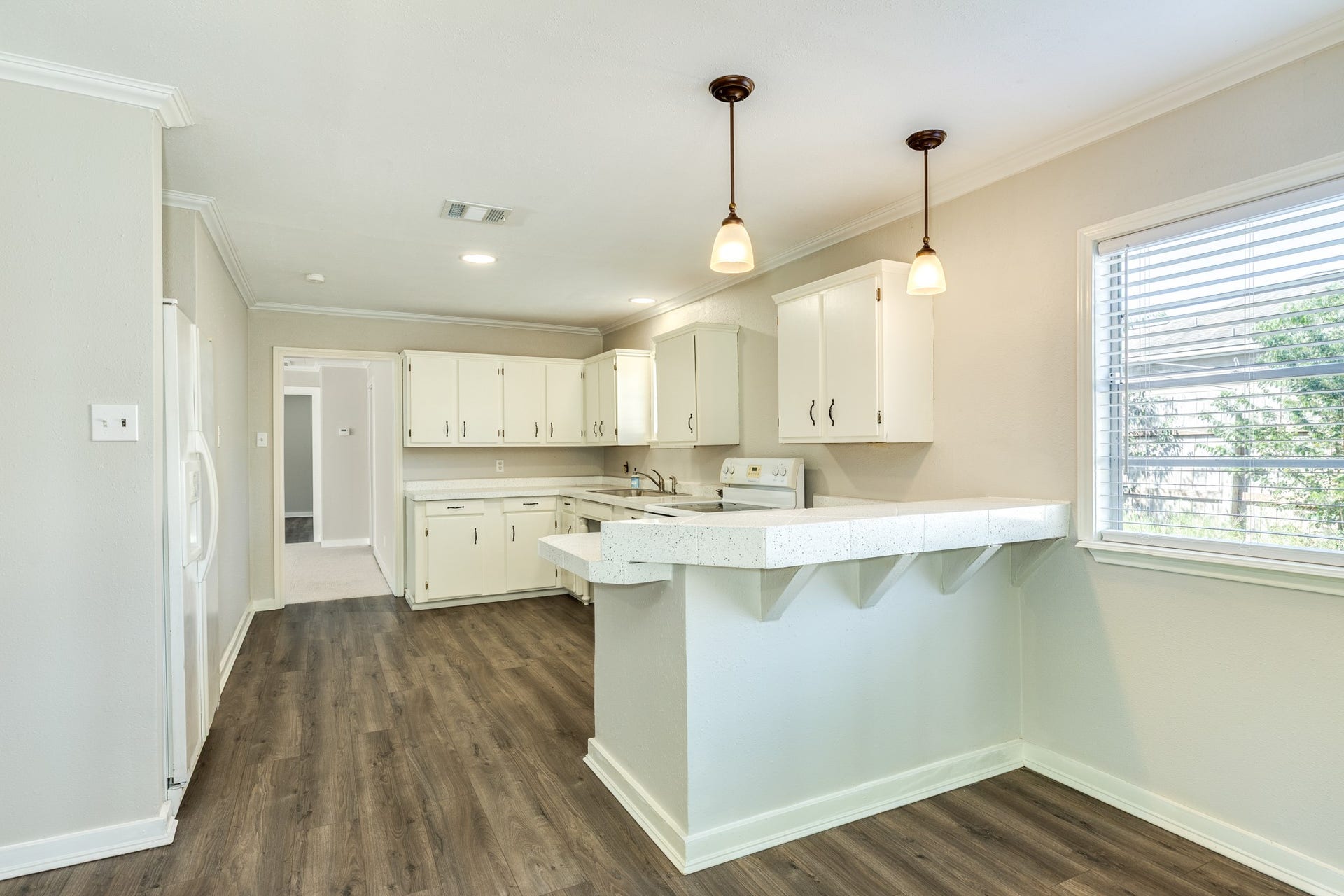 1602 County Road 939, Sweeny, TX 77480 Bright kitchen features white cabinetry, speckled countertops, and a spacious breakfast bar accented by pendant lighting. Wood-look flooring and a large window complement the inviting, functional layout.