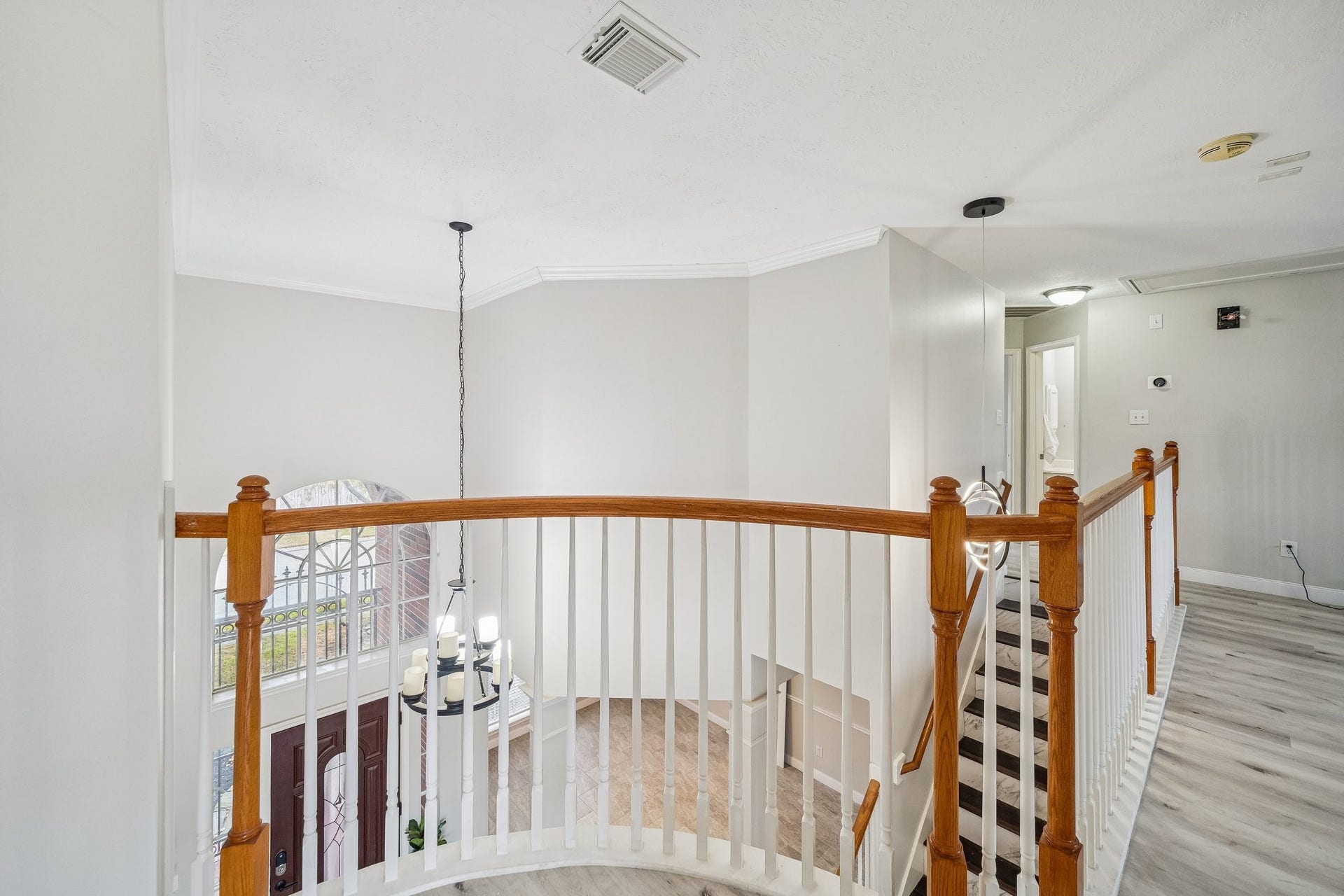 This photo showcases a bright, open hallway with a staircase featuring wooden railing and white balusters. The space is well-lit with a modern chandelier, and the light gray walls complement the sleek flooring. The layout suggests a welcoming, spacious interior.