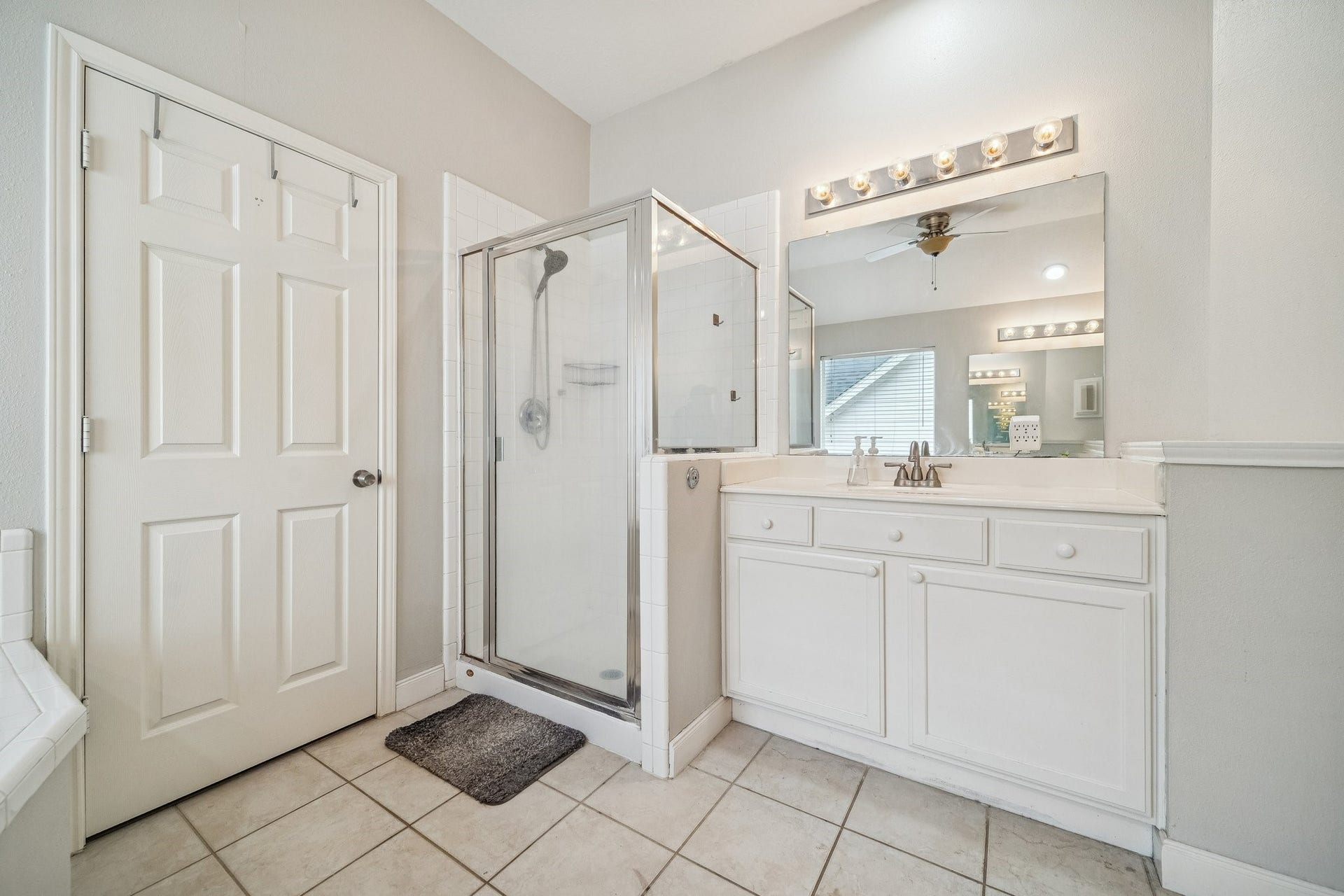 This bathroom features a modern glass-enclosed shower, a spacious vanity with ample storage, and bright lighting. Neutral tiles and light-colored walls create a fresh, clean look.