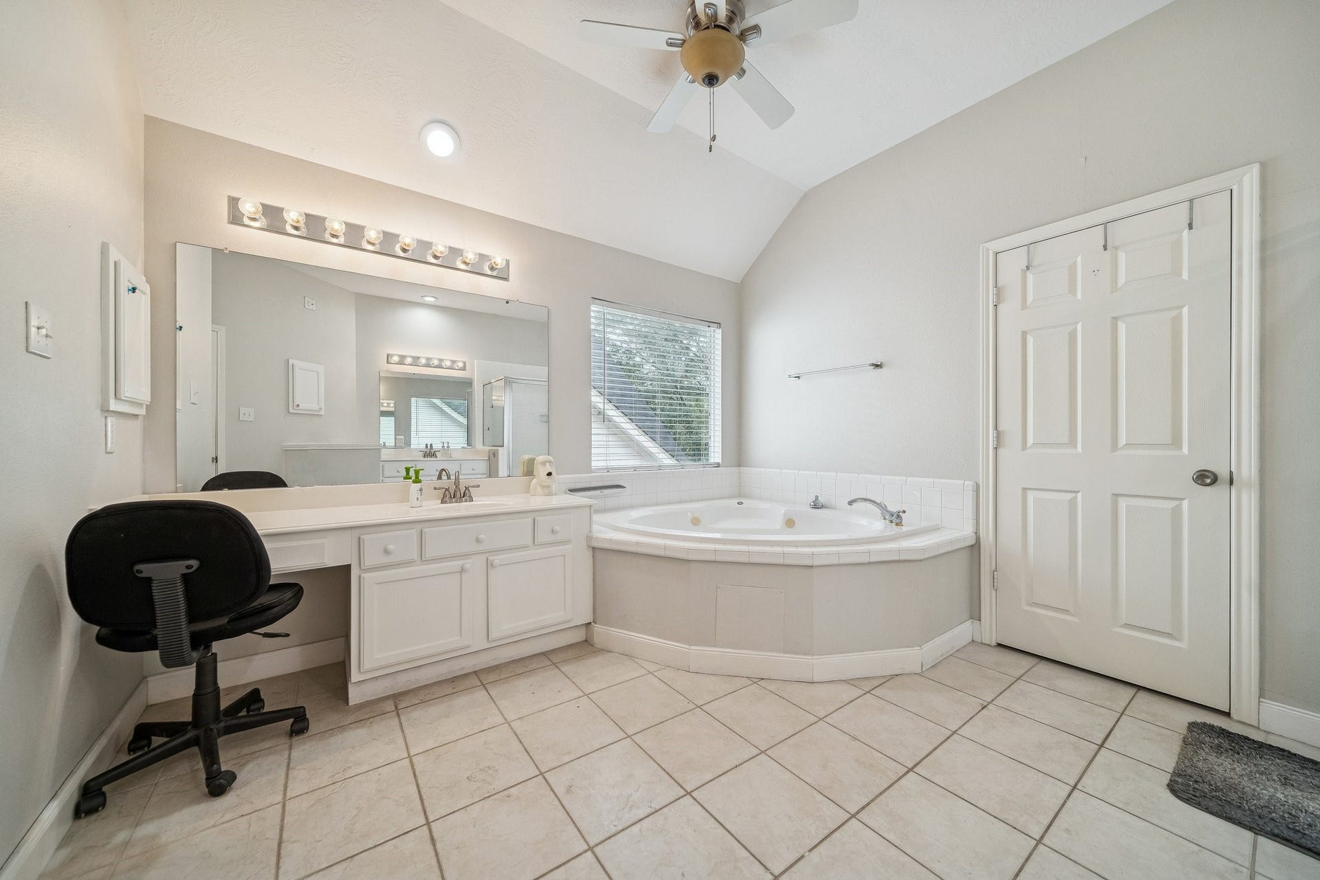 Bright bathroom with a corner jetted tub, large mirror, and vanity area. Features tiled floor, ample counter space, and natural light from a window.