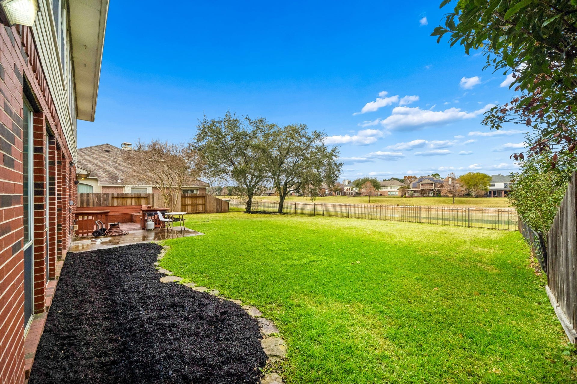 Spacious backyard with a lush green lawn, a patio for outdoor seating, and a view of neighboring homes. Ideal for relaxation and entertaining.