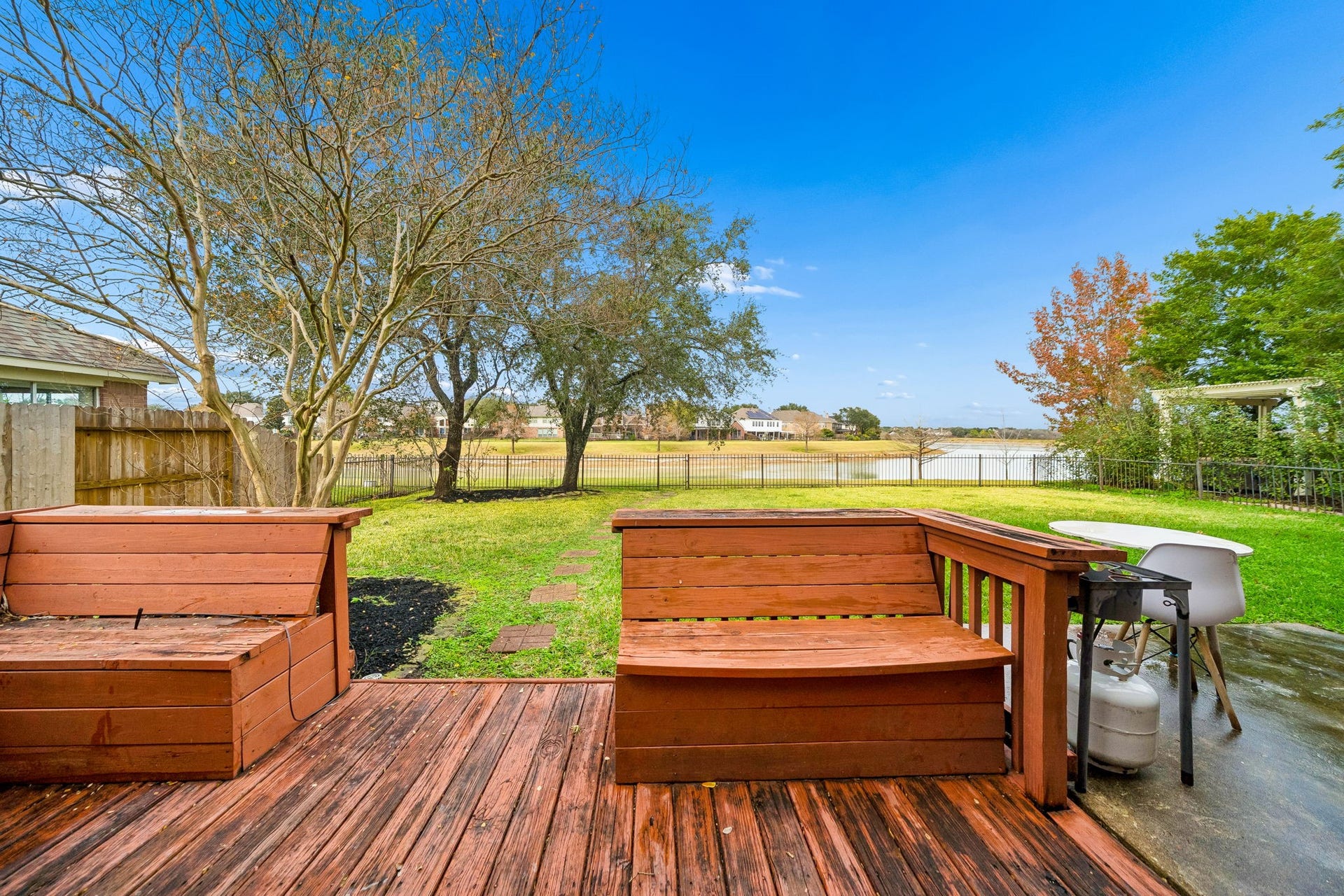 This backyard features a cozy wooden deck with built-in seating, overlooking a spacious lawn and a serene lake view. Ideal for relaxing and entertaining.