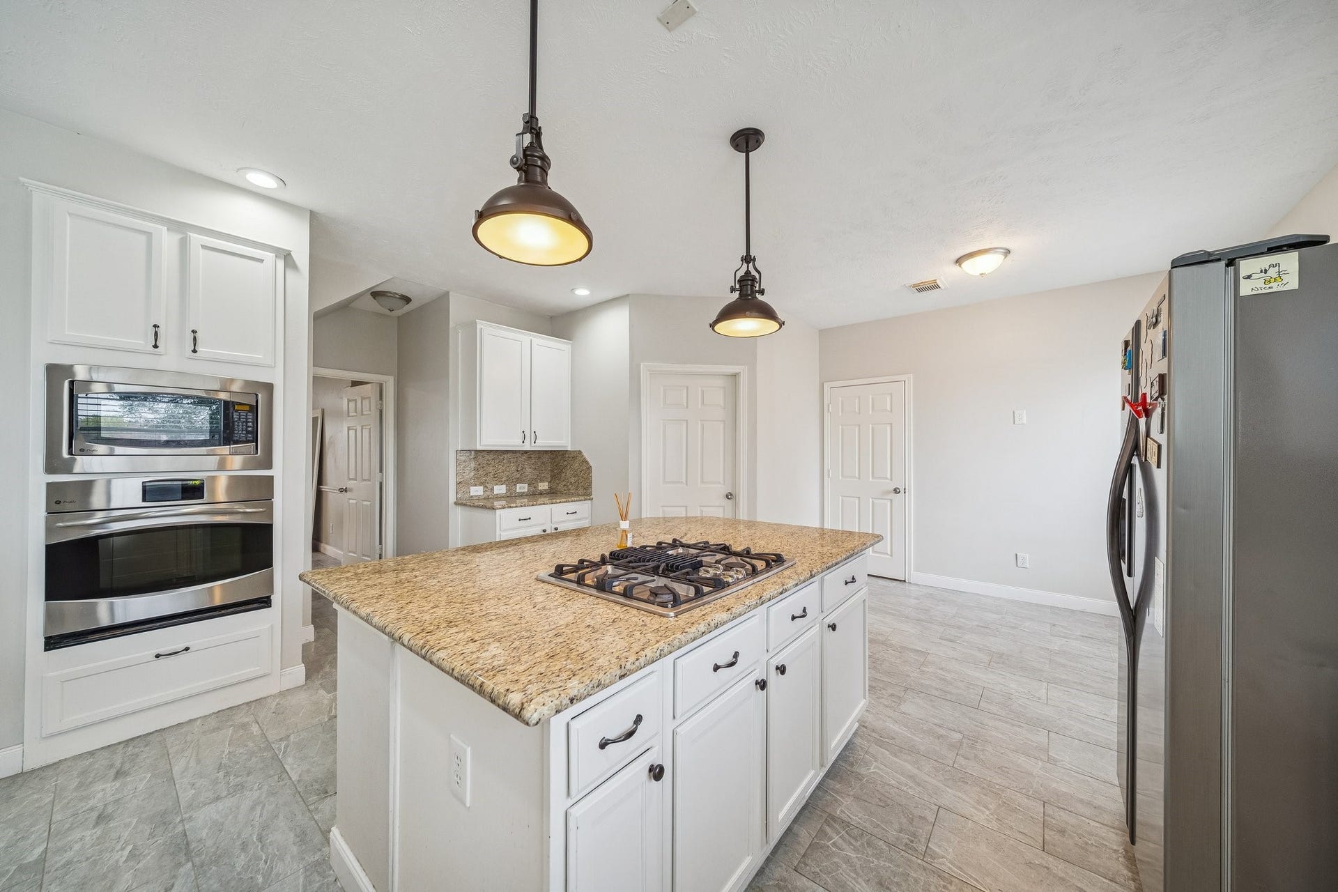 Modern kitchen with granite countertops, stainless steel appliances, and ample white cabinetry. Features a central island with a gas cooktop and stylish pendant lighting.