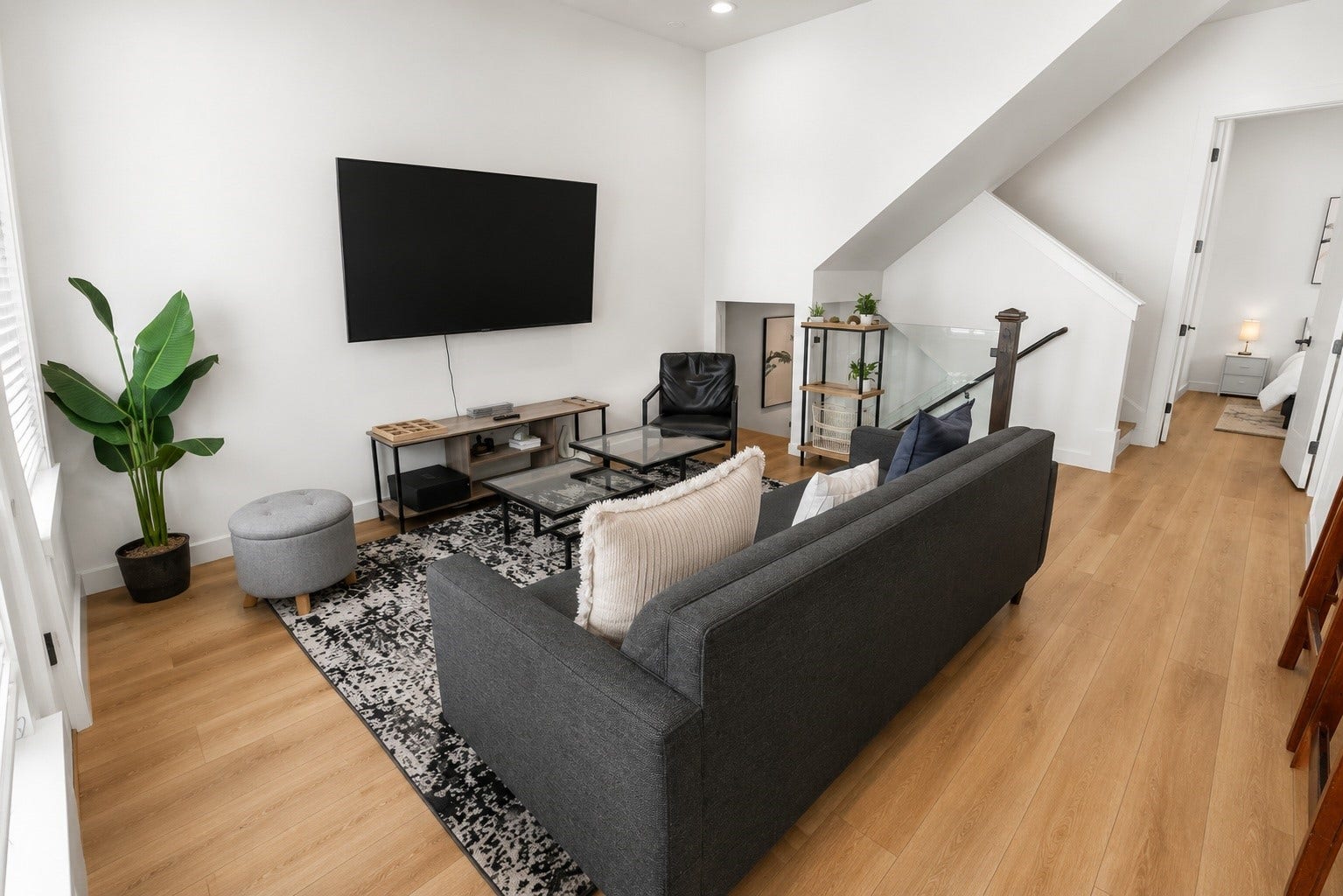 Gather, unwind, or entertain in a light filled living room where soaring ceilings and expansive windows create an open, airy atmosphere. Warm wood look flooring, contemporary finishes, and seamless access to the kitchen and staircase make this the natural gathering place of the home while maintaining a clean, sophisticated aesthetic.