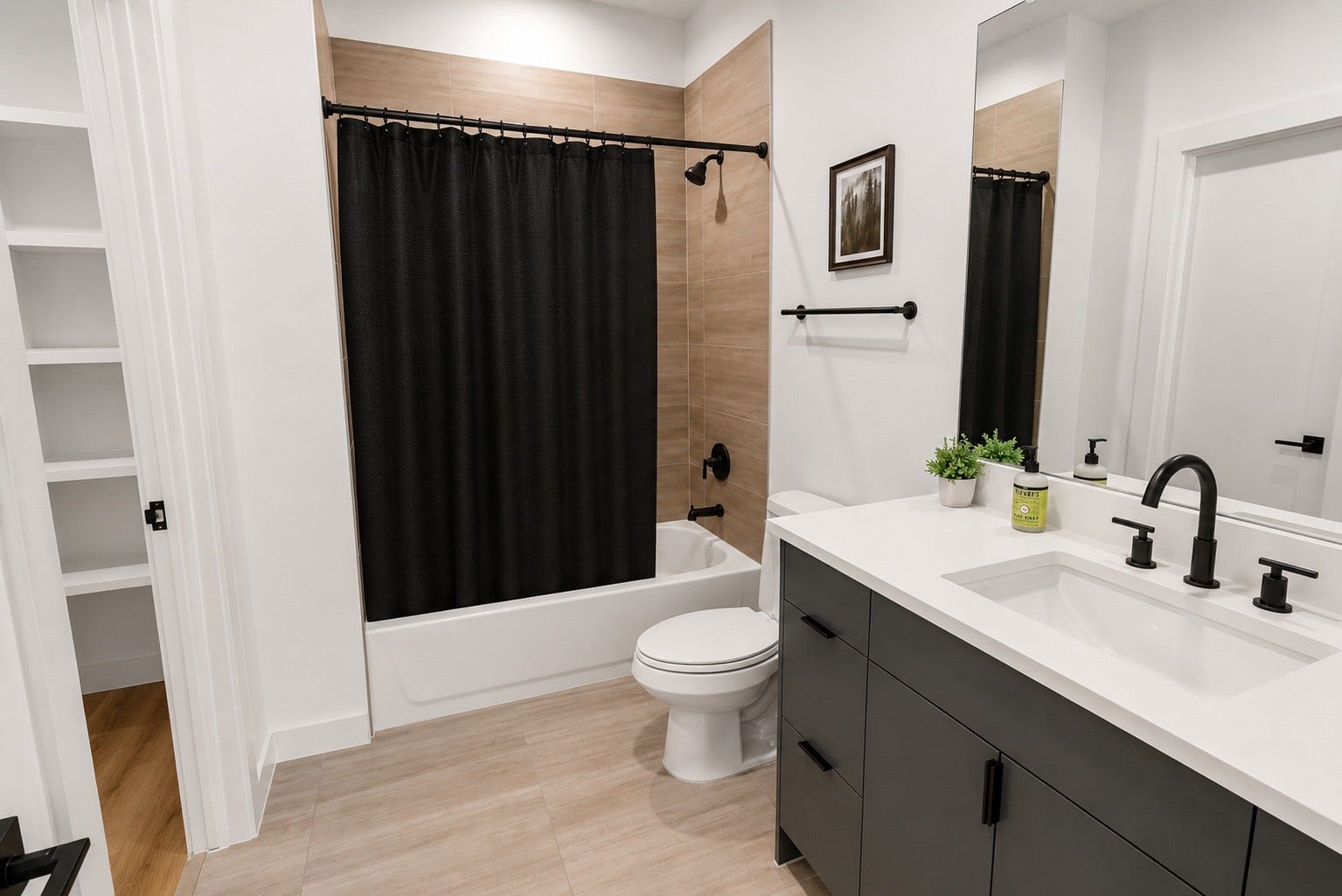 Contemporary en suite bath showcases quartz countertops, sleek gray cabinetry, matte black fixtures, and warm porcelain tile surrounding the tub and shower combination. Clean lines and timeless finishes create a polished space designed for both everyday comfort and lasting style.
