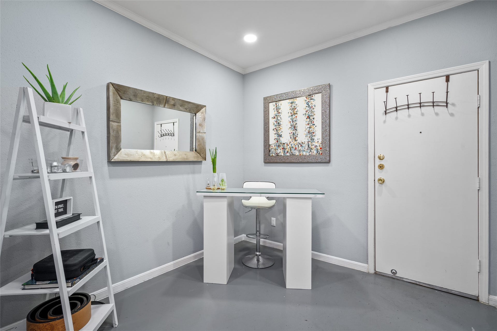 9850 Pagewood Lane, #1302, Houston, TX 77042 This inviting entryway doubles as a sleek and modern workspace. Love how the owners designed this area featuring a glass-top desk, a contemporary white barstool, and a decorative ladder shelf for stylish storage. Soft gray walls complement the rustic wood-framed mirror and abstract artwork, creating a welcoming and functional space.