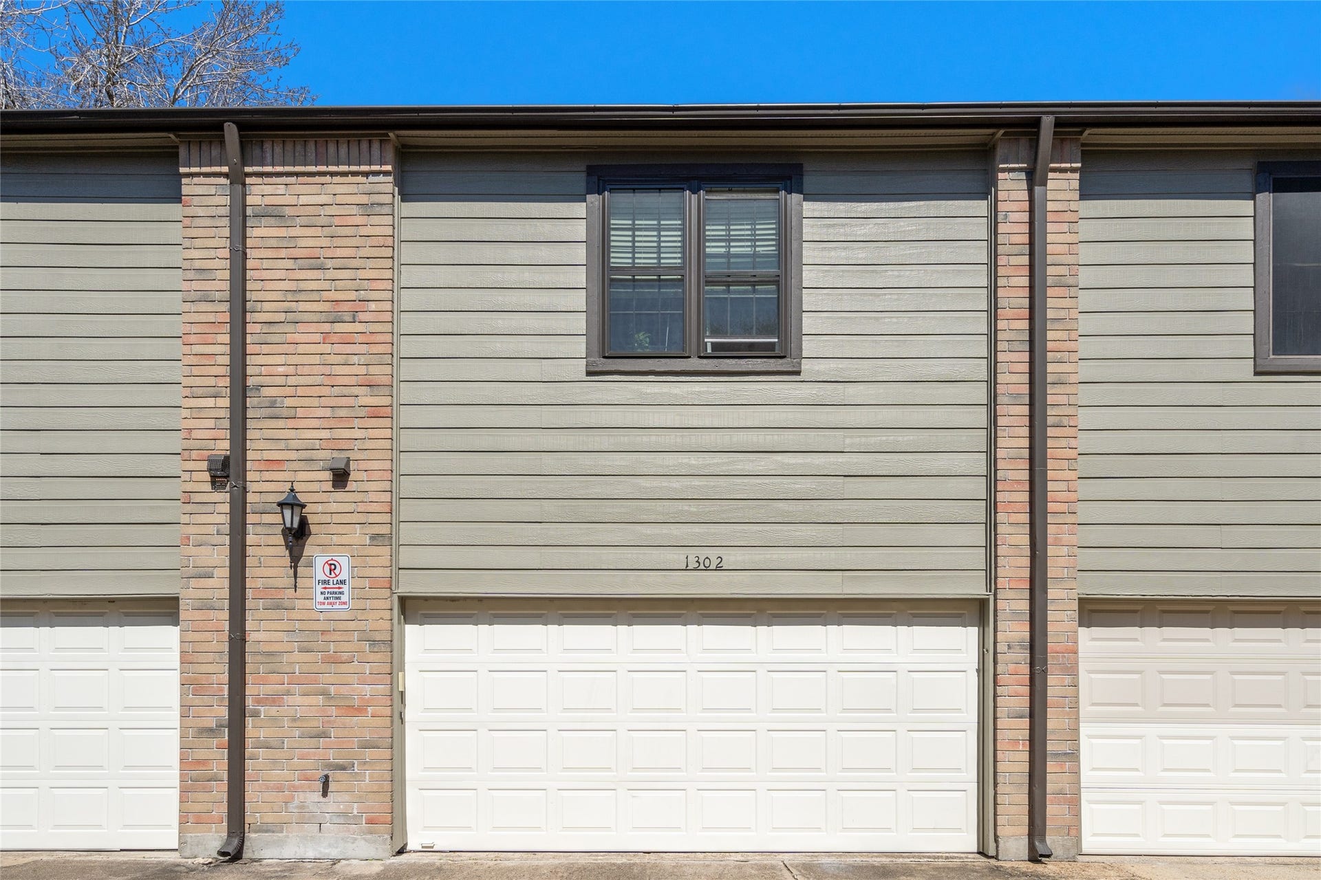 9850 Pagewood Lane, #1302, Houston, TX 77042 The rear of 9850 Pagewood Lane #1302 features a spacious two-car garage with a crisp white door, offering convenience and security. A blend of brick and modern siding gives the exterior a timeless yet updated look. The upper-level window allows for natural light, enhancing the home's inviting feel. A well-lit entry and clearly marked address add to the functionality of this charming townhome.