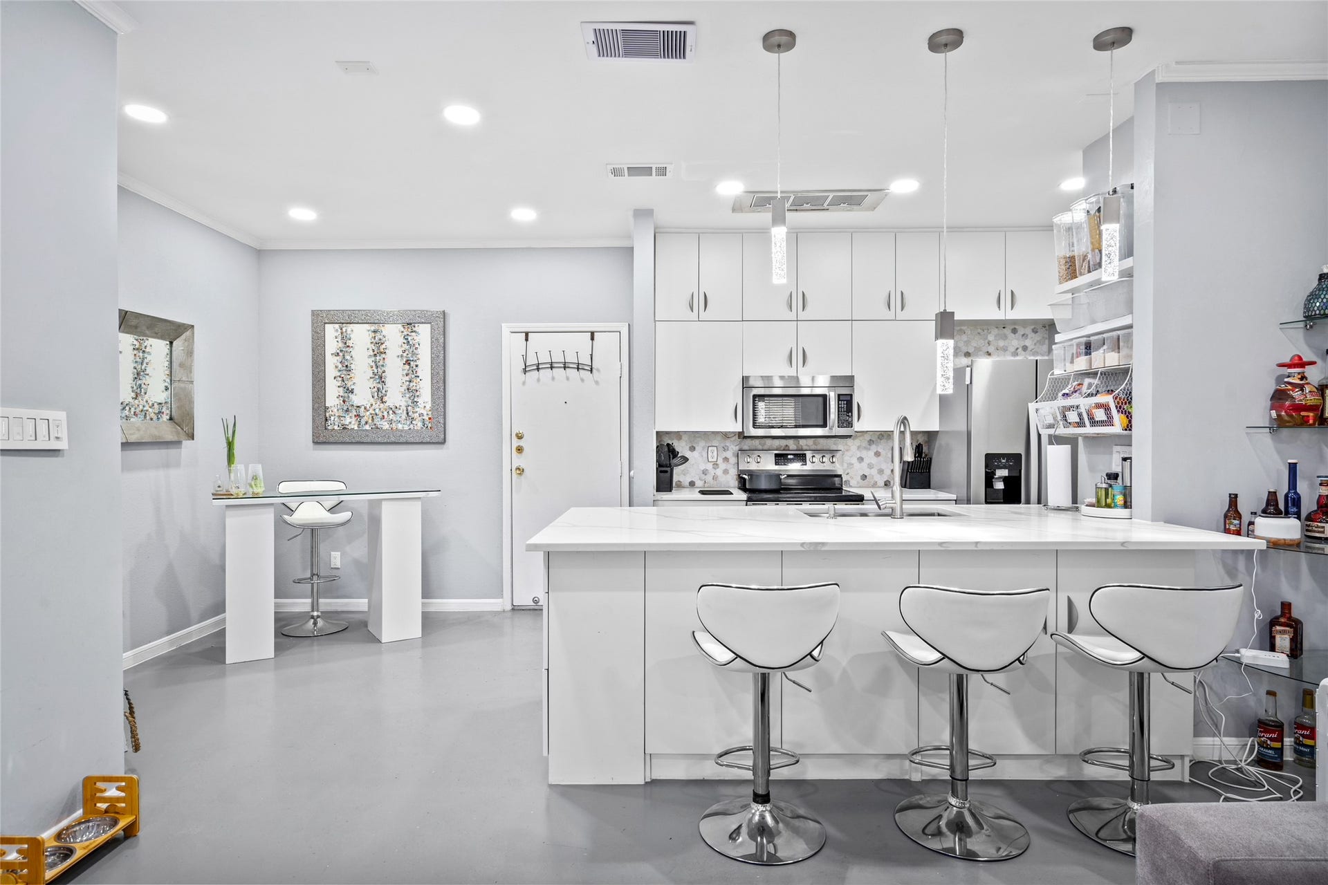 9850 Pagewood Lane, #1302, Houston, TX 77042 This stylish kitchen features crisp white cabinetry, stainless steel appliances, and a spacious island with a waterfall countertop, perfect for casual dining or entertaining. Elegant pendant lighting and a hexagonal tile backsplash add a contemporary touch, while open shelving provides functional storage. The seamless flow into the living area makes this kitchen both inviting and practical.