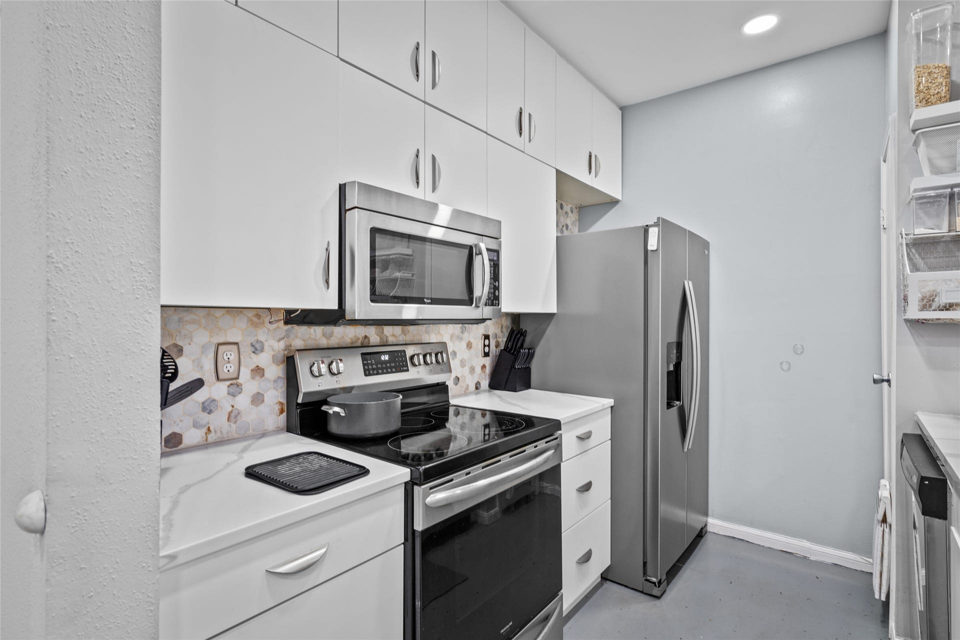 9850 Pagewood Lane, #1302, Houston, TX 77042 This compact yet highly functional kitchen showcases crisp white cabinetry, a stylish hexagonal backsplash, and quartz countertops. Stainless steel appliancesincluding a microwave, electric range, and spacious refrigeratorprovide modern convenience, while ample overhead cabinets maximize storage. The clean, streamlined design makes meal prep and cooking a breeze.