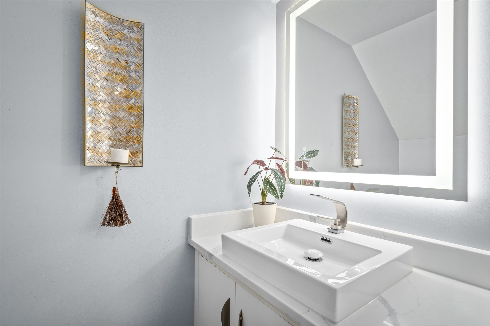 9850 Pagewood Lane, #1302, Houston, TX 77042 This elegant downstairs half bath features a modern vessel sink atop a sleek quartz countertop. A backlit mirror adds a contemporary touch, while the neutral tones and decorative wall accents create a warm and inviting space. Perfect for guests, this thoughtfully designed powder room combines function and style.