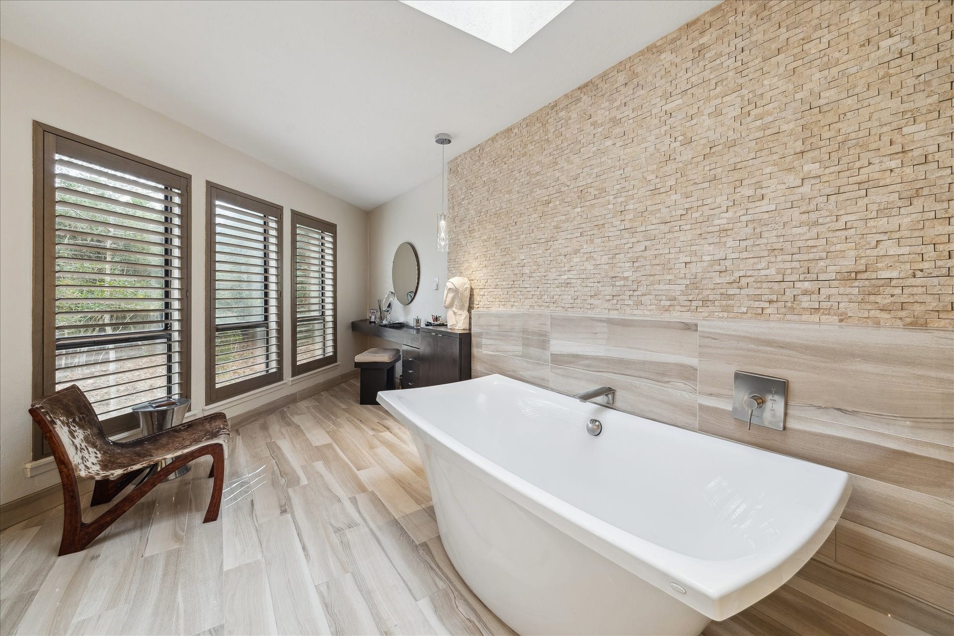 23414 Holly Hollow Street, Tomball, TX 77377 A soaking tub set against a dramatic stone accent wall, bathed in natural light from the skylight, complemented by a sophisticated separate vanity area designed for ultimate relaxation.