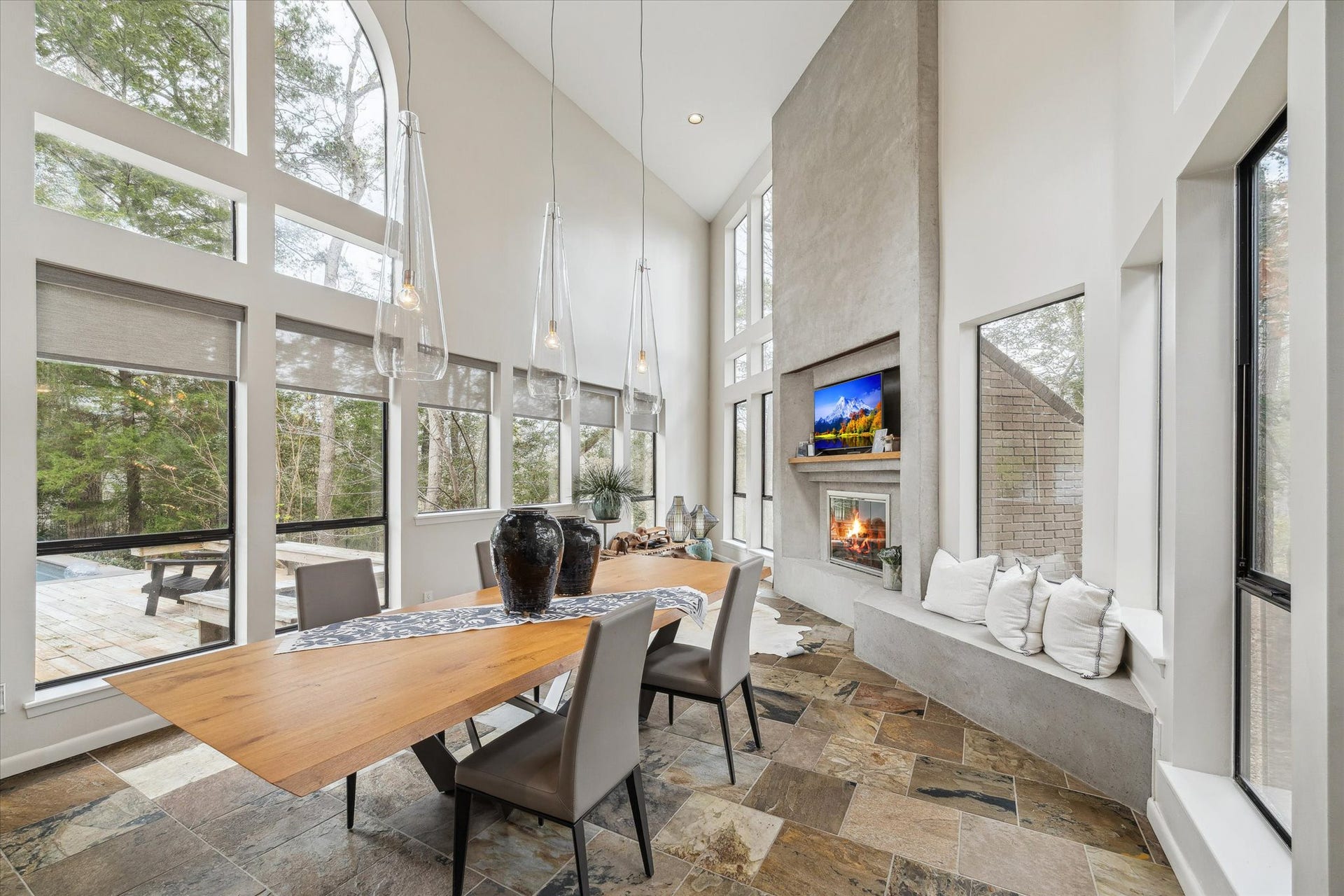 23414 Holly Hollow Street, Tomball, TX 77377 Dramatic, light-filled casual dining space featuring soaring ceilings and expansive windows that frame serene wooded views. The open-concept design is highlighted by floor-to-ceiling glass, sleek modern lines, and an abundance of natural light throughout.