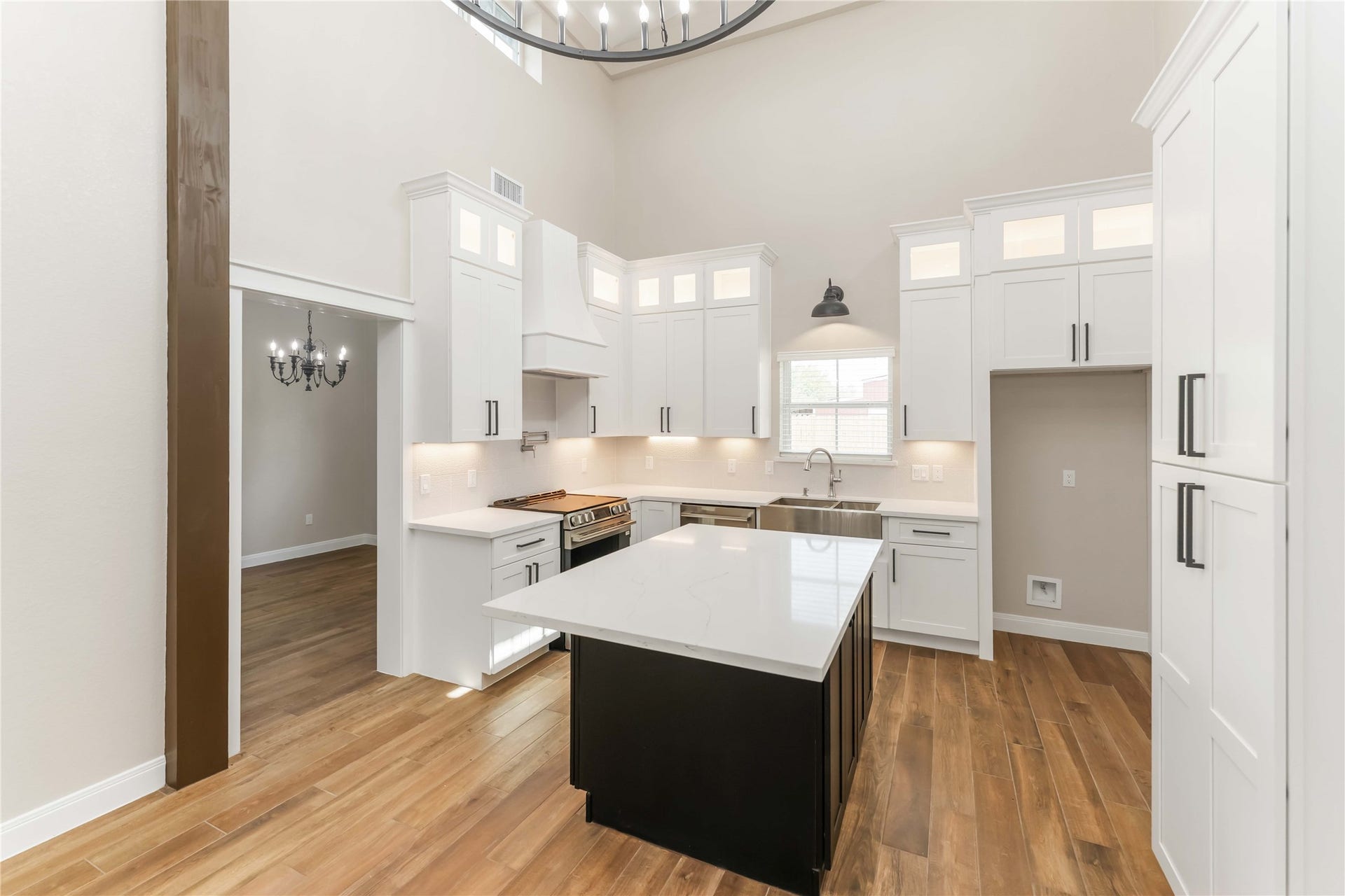 4864 County Road 182 Off, Alvin, TX 77511 This bright, modern kitchen features high ceilings, white cabinetry with ample storage, and a large central island with a sleek countertop. A stainless steel farmhouse sink and high-end appliances complete the space, complemented by warm tile wood-style flooring and contemporary lighting.