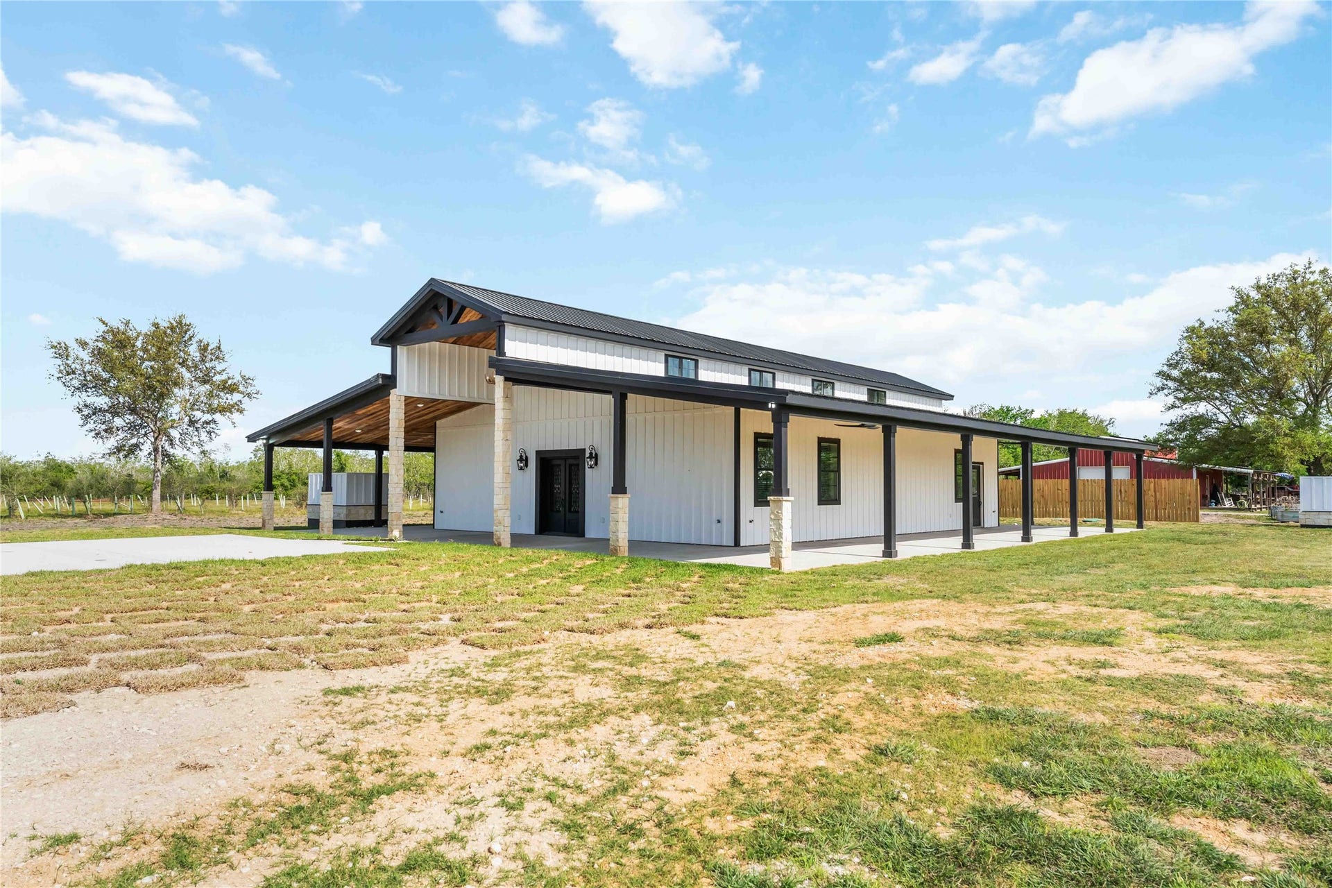 4864 County Road 182 Off, Alvin, TX 77511 Modern farmhouse with a sleek black and white exterior, expansive covered porch, and surrounded by open land. Ideal for those seeking a blend of rustic charm and contemporary design.
