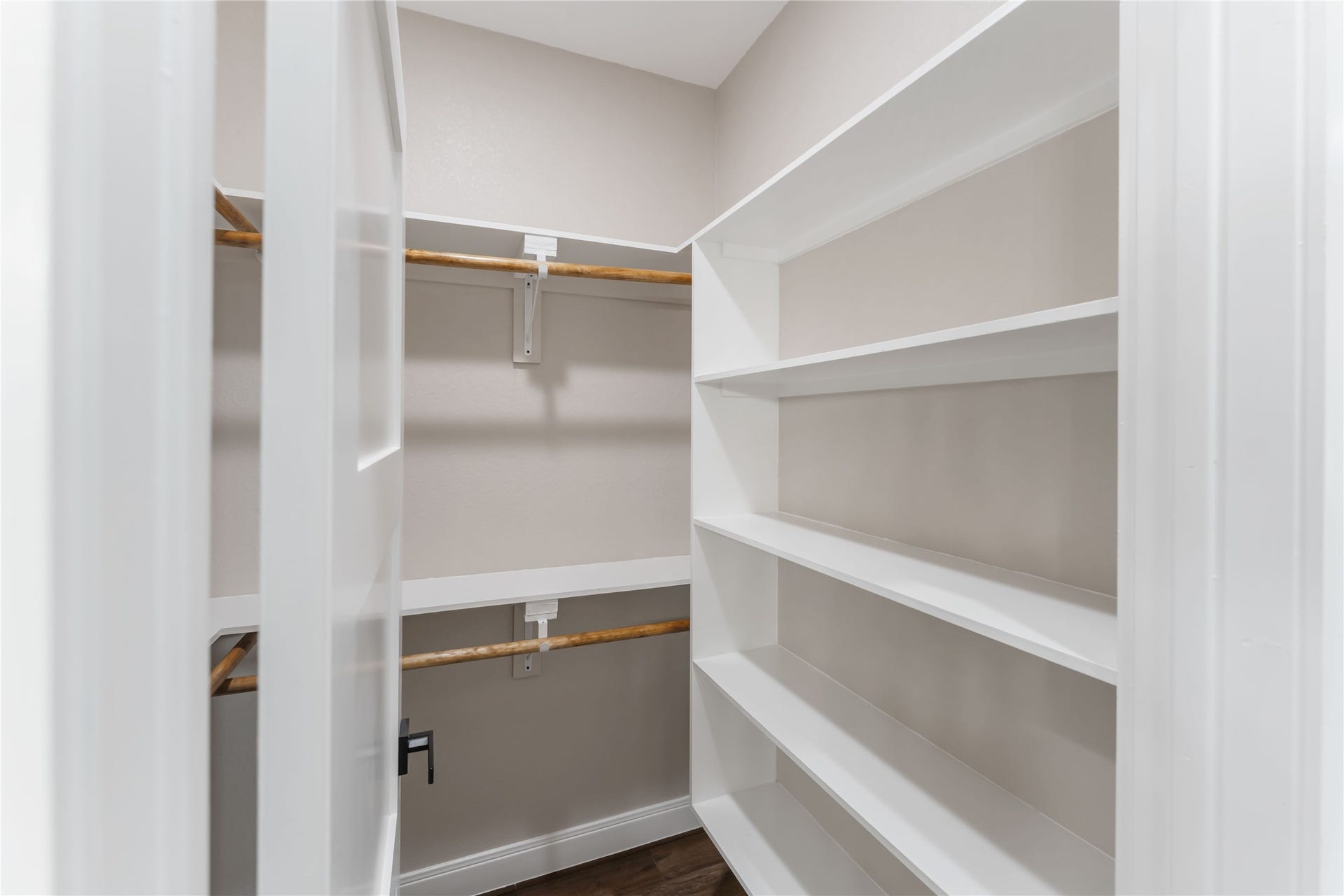 4864 County Road 182 Off, Alvin, TX 77511 This photo shows a walk-in closet with white shelving on the right and wooden hanging rods on the left. The space is well-organized, providing ample storage for clothes and other items.