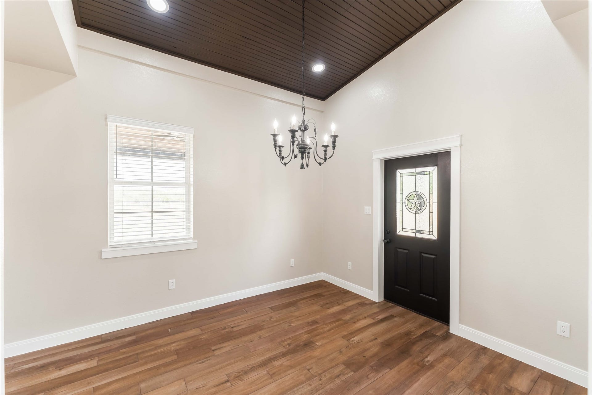 4864 County Road 182 Off, Alvin, TX 77511 This room features a warm tile wood-style floor and a dark wood ceiling with recessed lighting. It includes a stylish chandelier and a decorative front door with glass detailing, complemented by a window that lets in natural light.