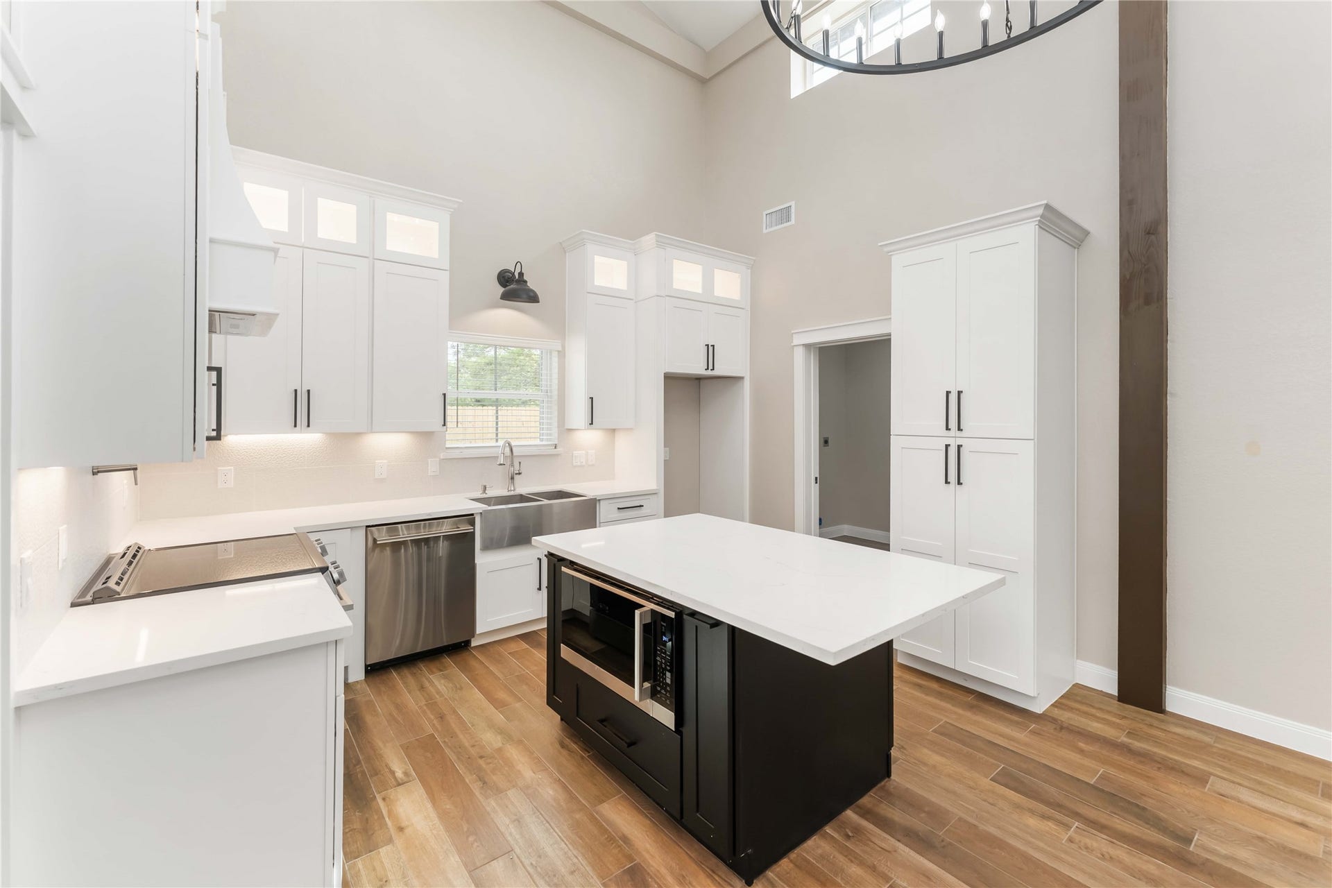 4864 County Road 182 Off, Alvin, TX 77511 This modern kitchen features high ceilings, white cabinetry, and stainless steel appliances. It includes a central island with a built-in oven and a farmhouse sink. The space is bright with natural light and has tile wood-style flooring.