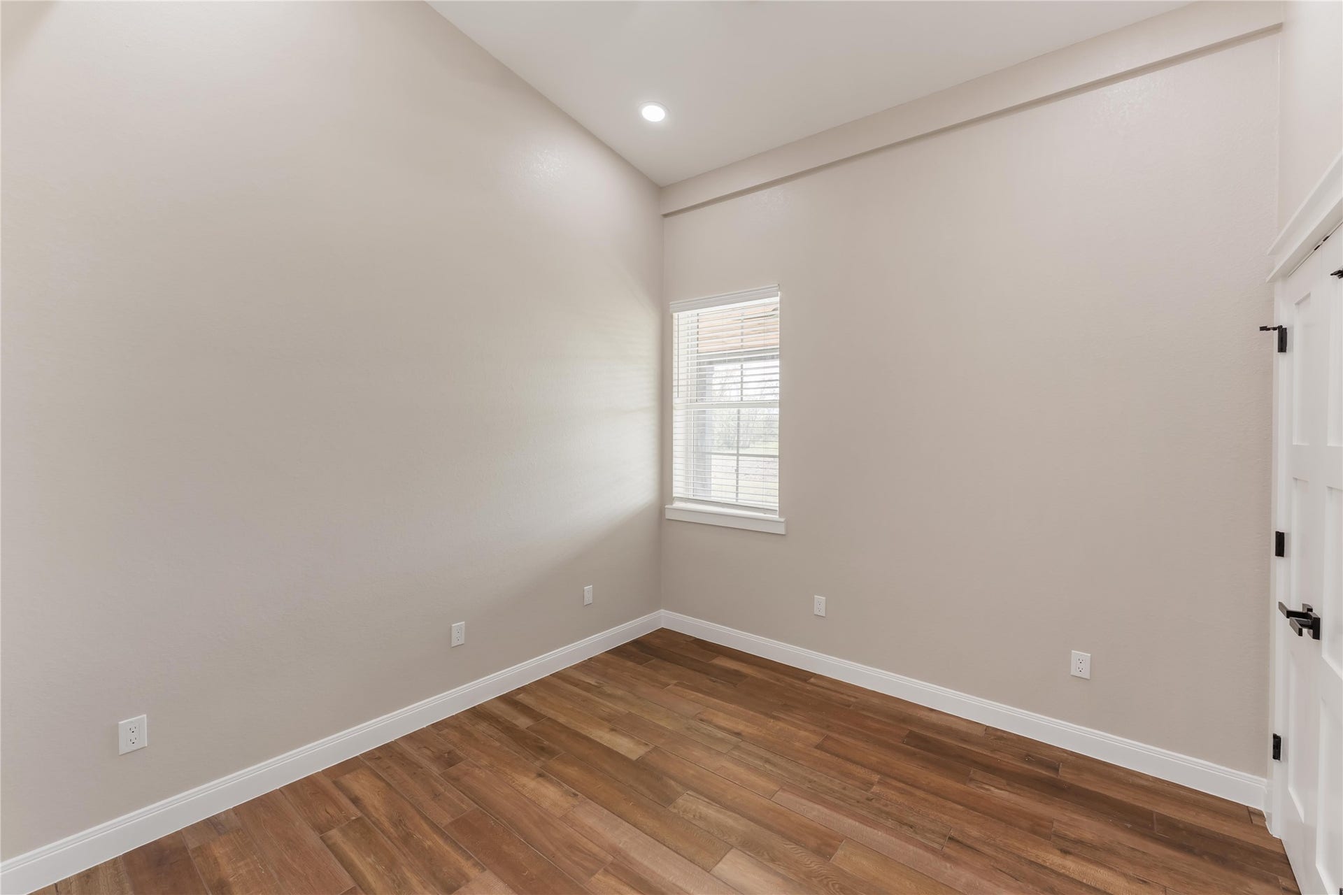 4864 County Road 182 Off, Alvin, TX 77511 This room features neutral taupe walls, tile wood-style flooring, and a high ceiling with recessed lighting. A window provides natural light, and there's a white door with modern hardware.