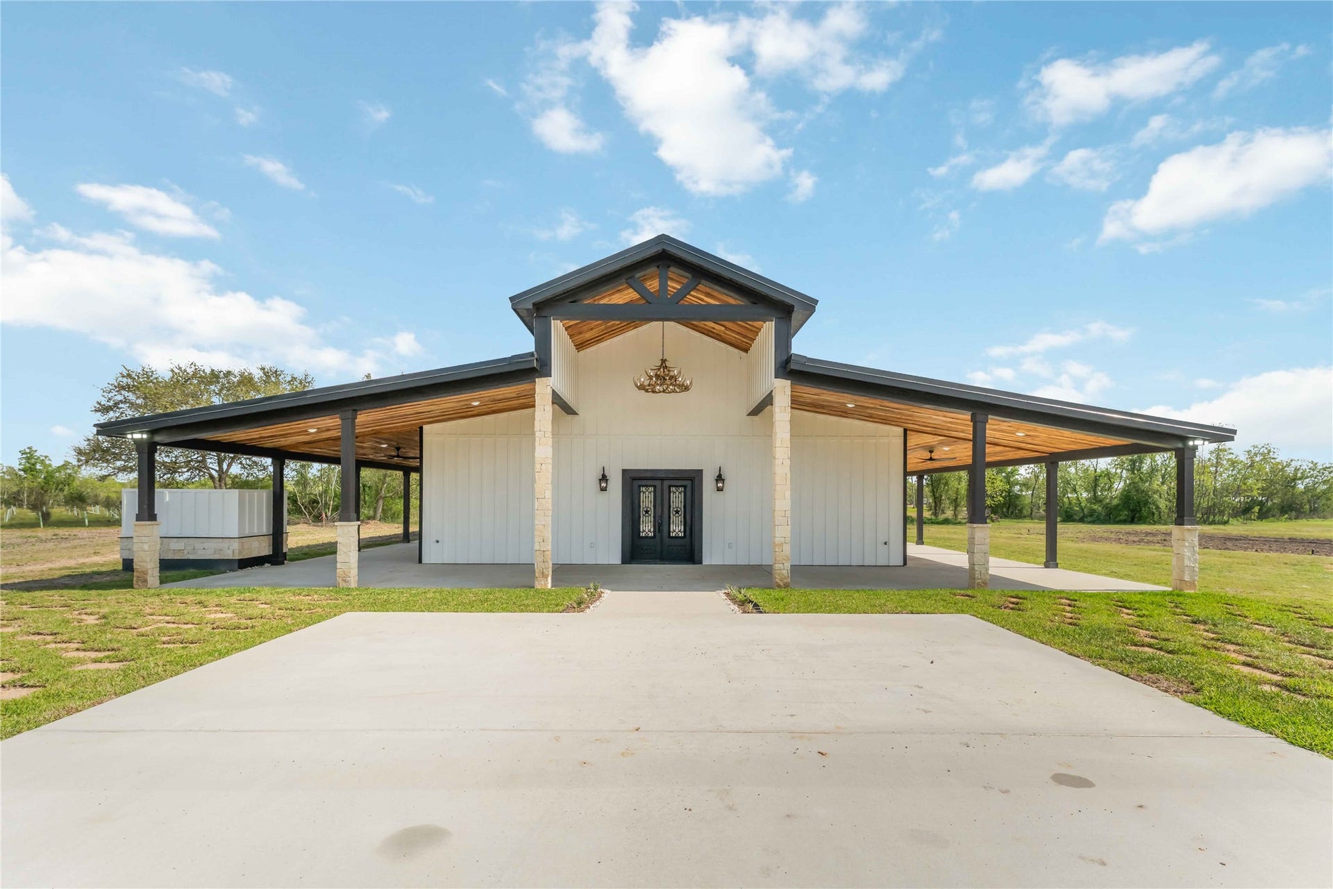 4864 County Road 182 Off, Alvin, TX 77511 This photo showcases a modern farmhouse-style home with a spacious covered porch, high ceilings, and a sturdy metal roof, set on a large plot of land. Perfect for enjoying open-air living in a rural setting.