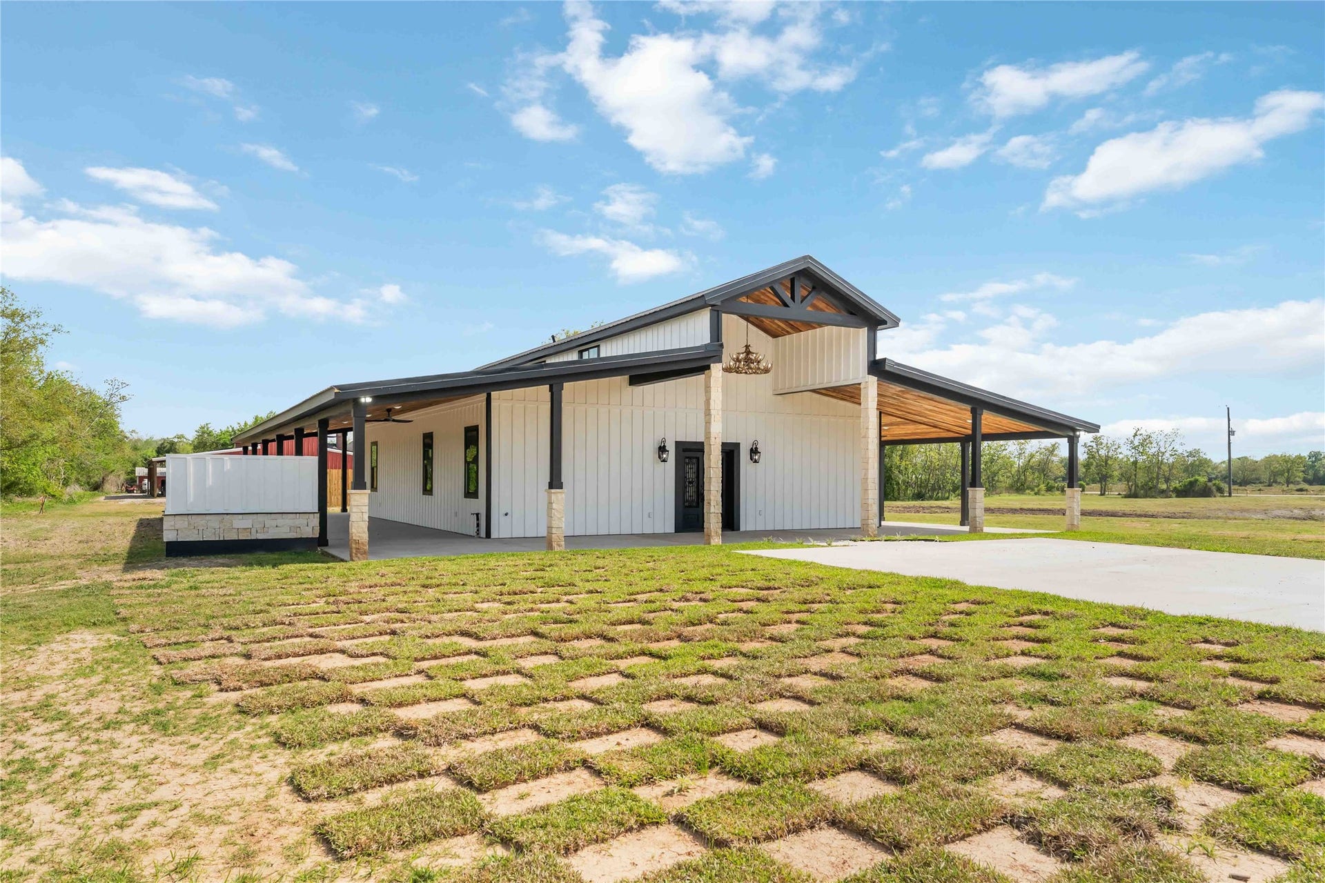 4864 County Road 182 Off, Alvin, TX 77511 This modern farmhouse features a spacious, open design with a blend of rustic and contemporary elements. It boasts a large covered porch, ample natural light, and a rustic wood and metal exterior, set against a backdrop of open land. Perfect for those seeking a blend of style and tranquility.