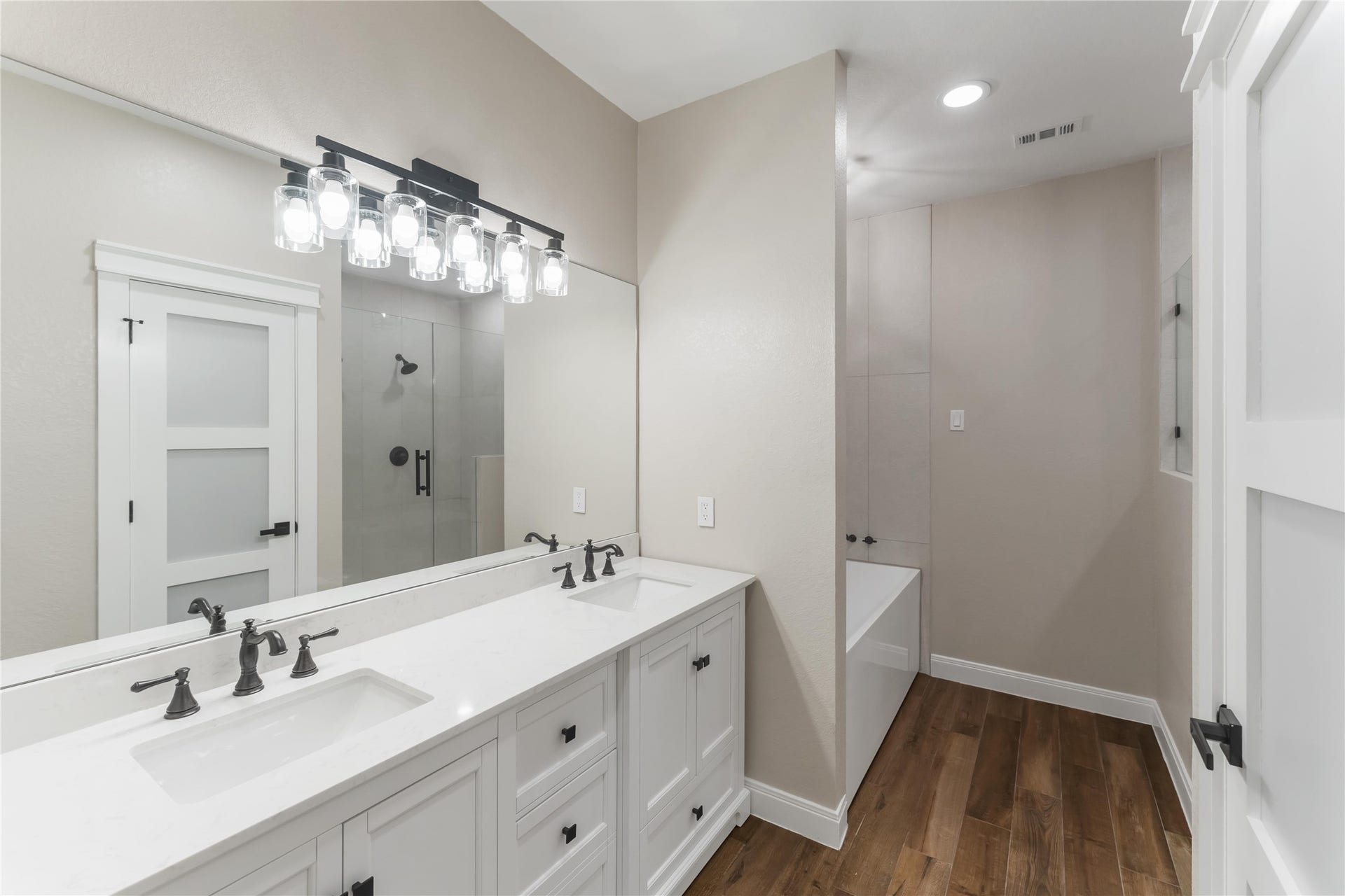 4864 County Road 182 Off, Alvin, TX 77511 This bathroom features a modern double vanity with sleek black fixtures, a large mirror, and stylish lighting. It includes a spacious glass-enclosed shower and a separate bathtub, all set on elegant tile wood-style flooring.