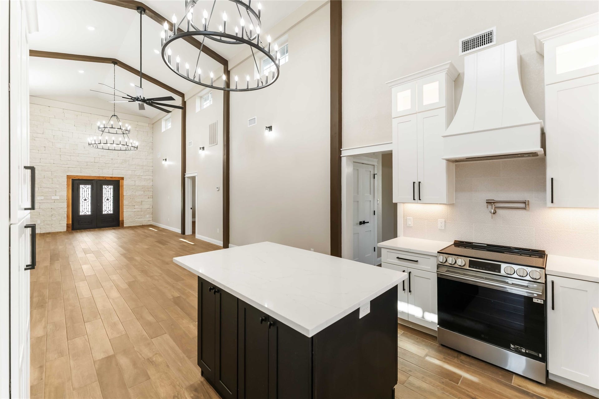 4864 County Road 182 Off, Alvin, TX 77511 This spacious and elegant open-concept living area features high ceilings, modern chandeliers, and a stone accent wall. The kitchen boasts sleek cabinetry, a central island, and stainless steel appliances, all complemented by warm wood look tile flooring.