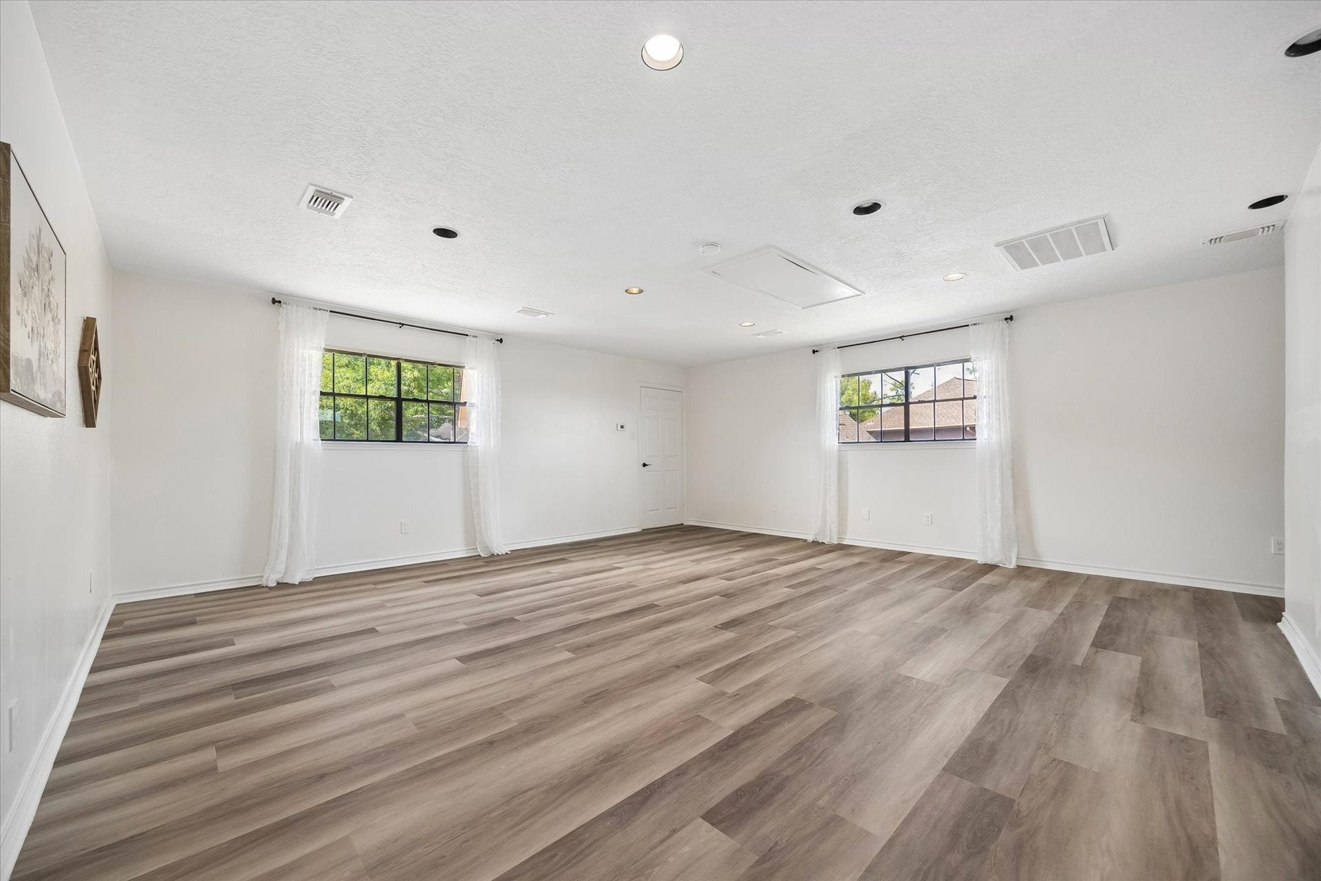 Spacious, light-filled room with sleek wood flooring and large windows, perfect for versatile living.