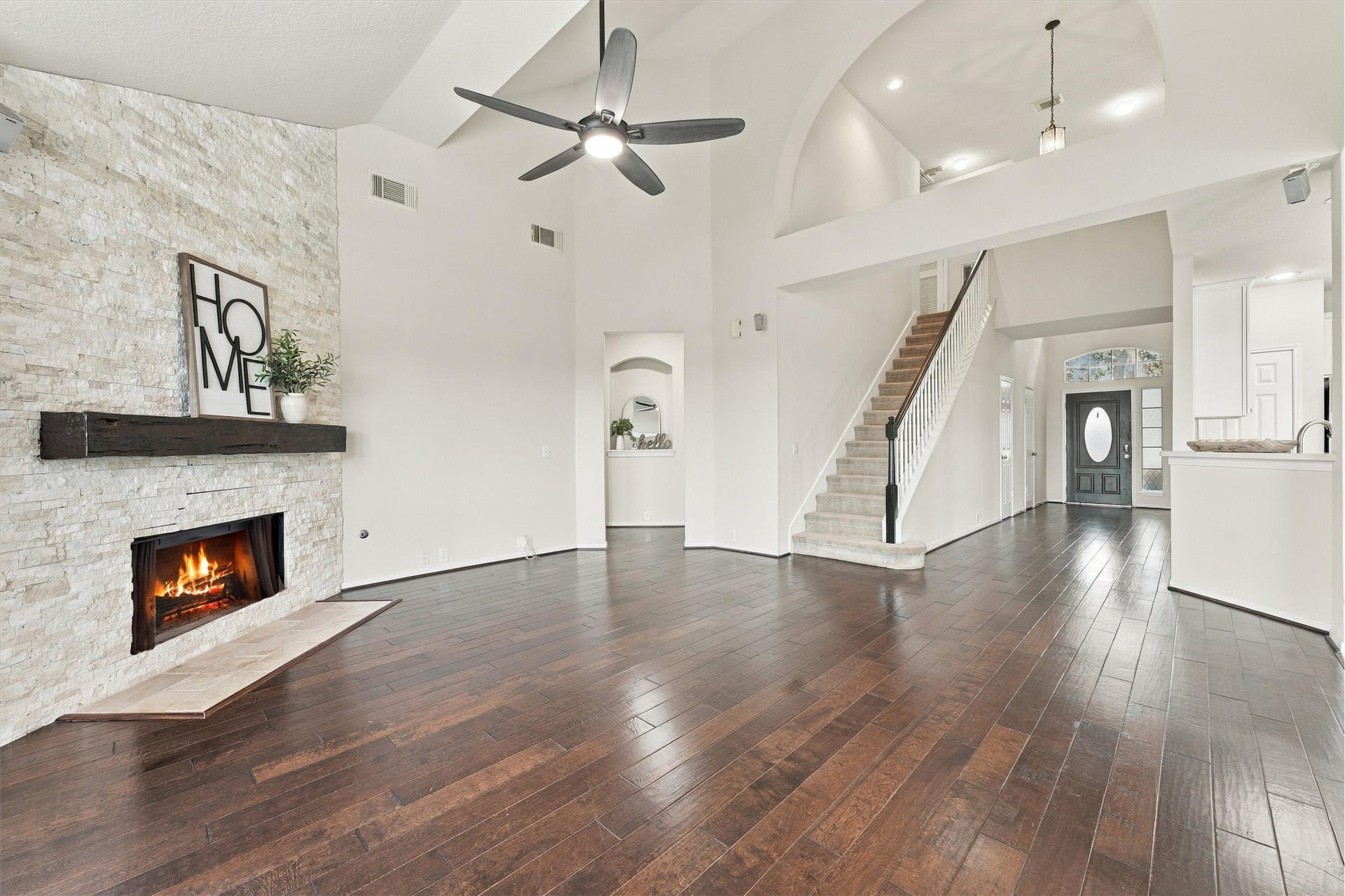 Expansive family room featuring soaring ceilings, engineered hardwood flooring, and a stunning stacked stone fireplace.