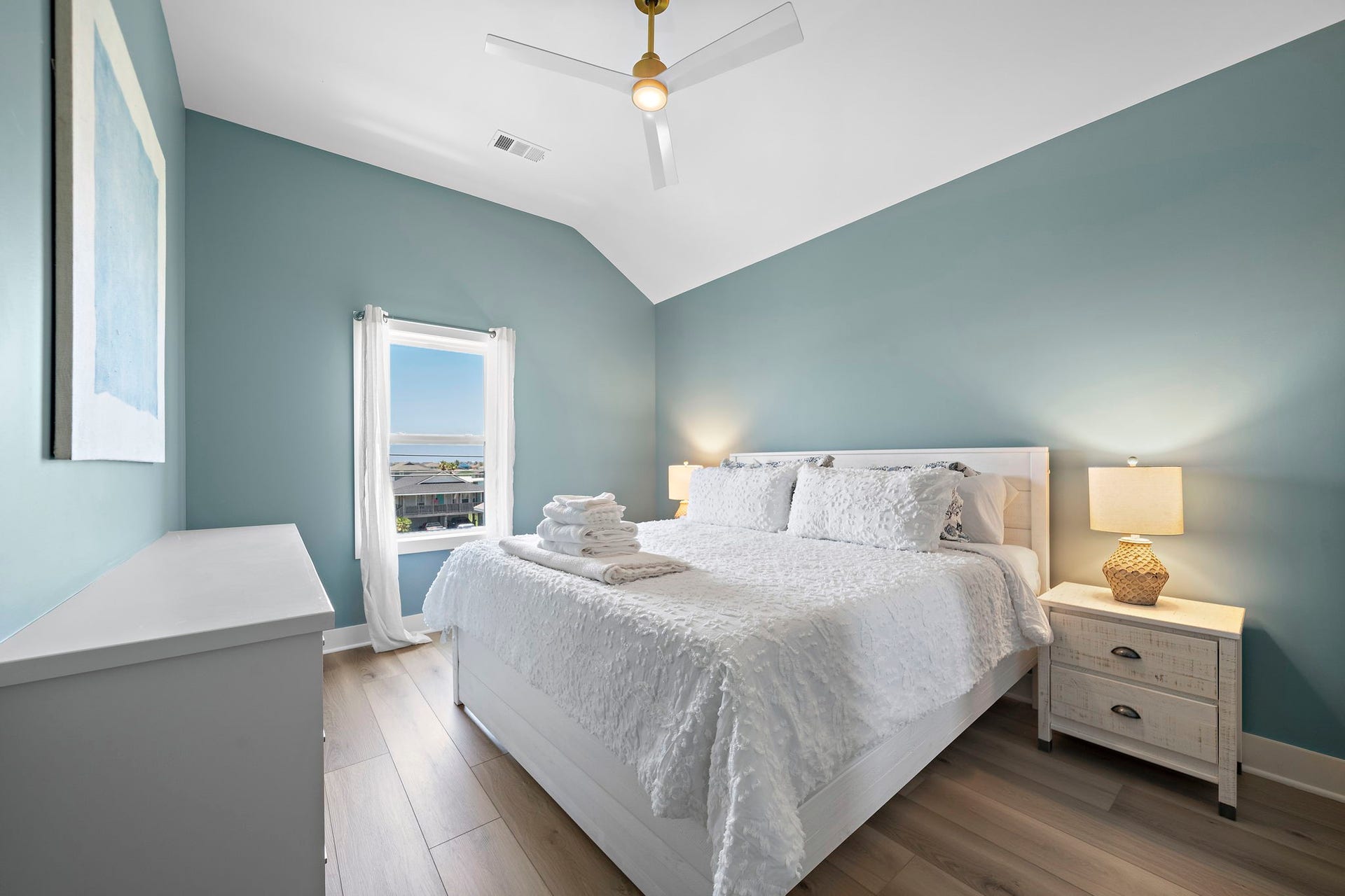 Serene bedroom with soothing blue walls, a comfortable bed, and ample natural light from a well-placed window, creating a cozy and inviting atmosphere.