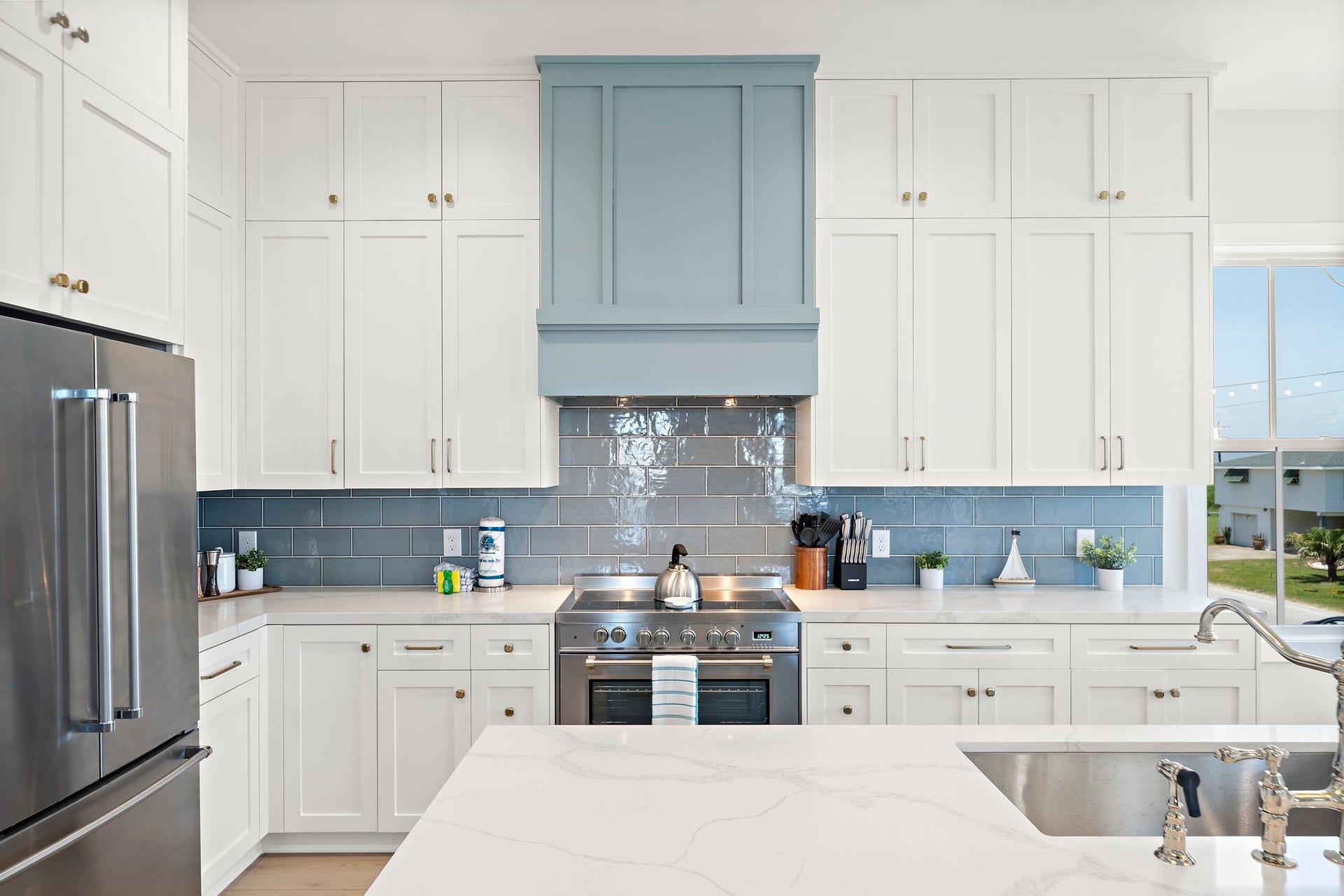 Bright and inviting kitchen with sleek stainless steel appliances, elegant white cabinetry, and a stylish blue tile backsplash.