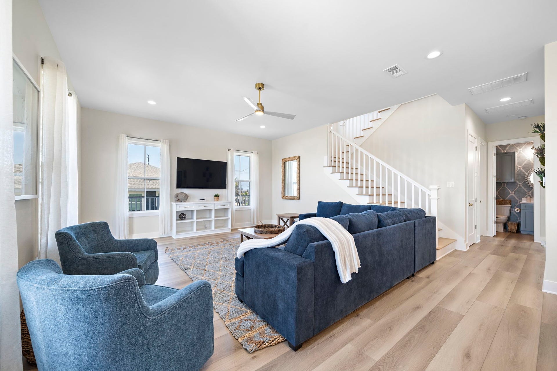 Bright and spacious living room featuring elegant hardwood floors, a plush blue sectional, and modern accents, complemented by a stylish ceiling fan and ample natural light.