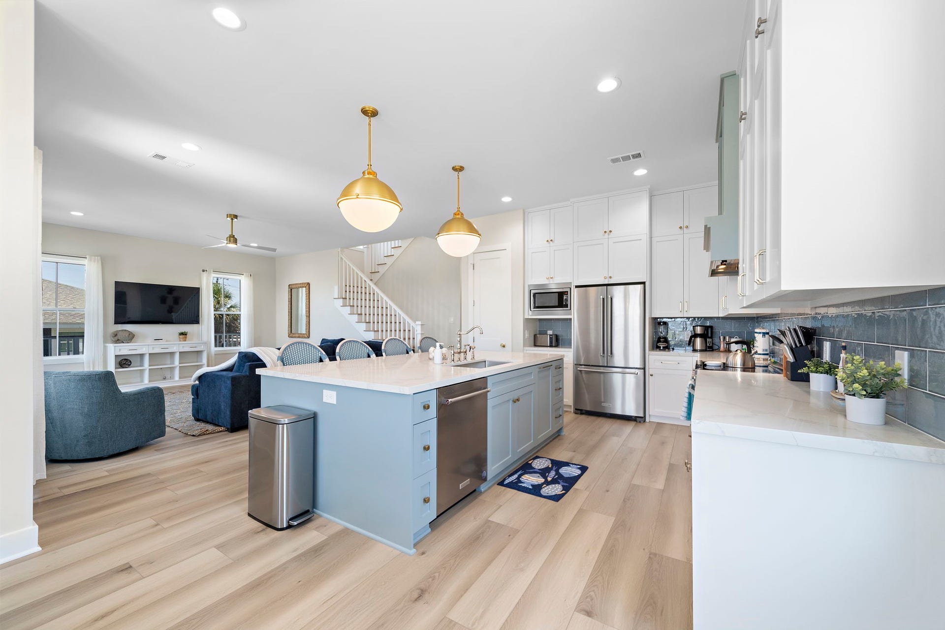 Spacious open-concept kitchen and living area featuring a large island with elegant pendant lighting, stainless steel appliances, and ample cabinetry, seamlessly flowing into a cozy living room with a modern staircase.