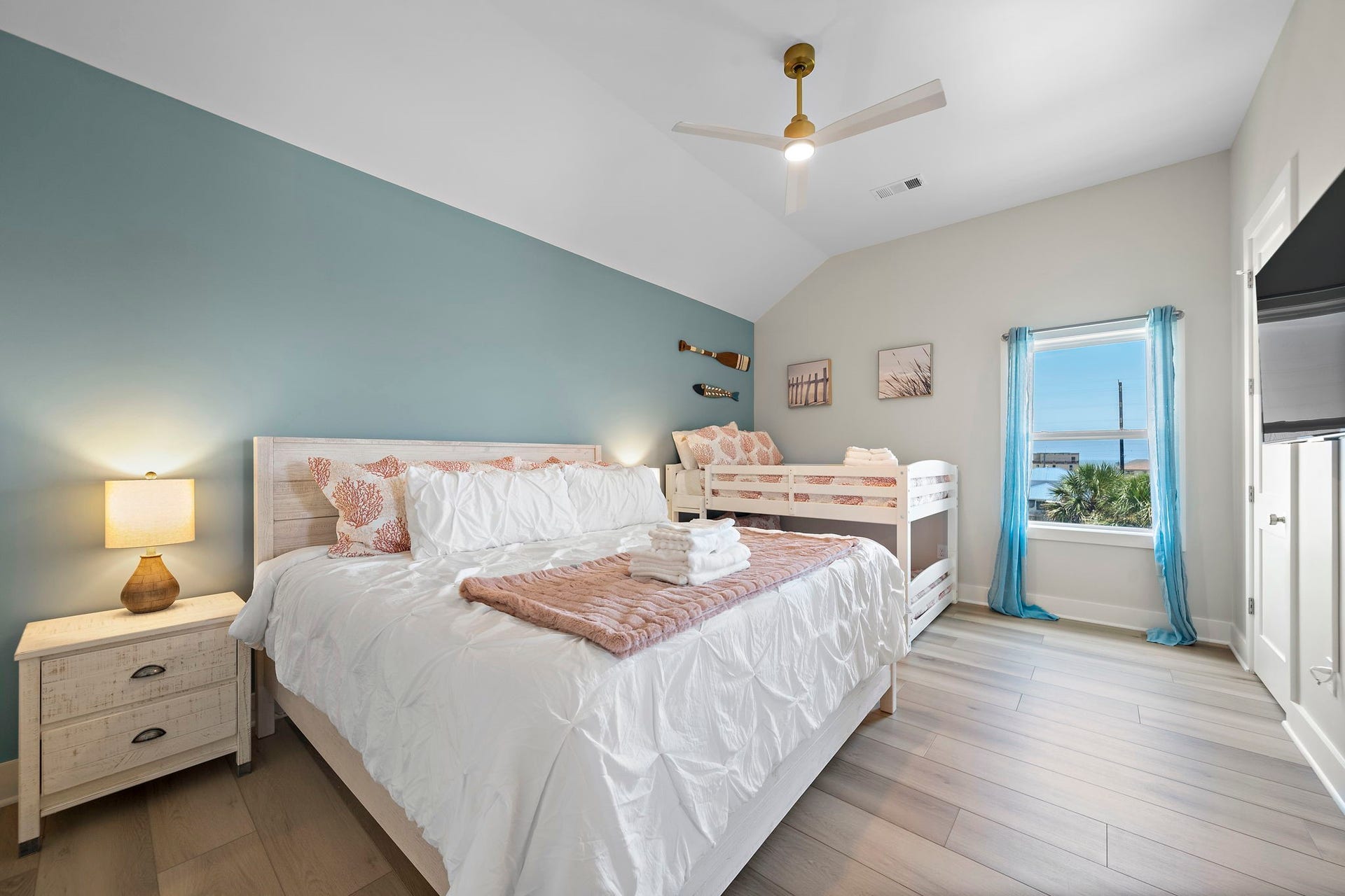 Spacious bedroom with a serene blue accent wall, featuring a cozy king-sized bed and a charming bunk bed. Large window offers stunning water views, filling the room with natural light.