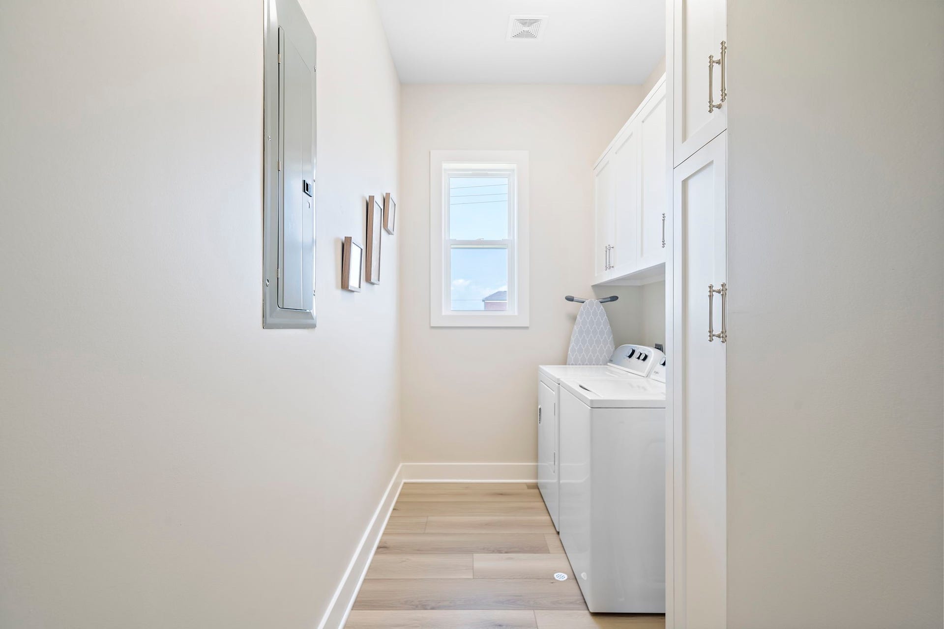 Bright and efficient laundry room featuring sleek white cabinetry, modern washer and dryer, and natural light from the window.