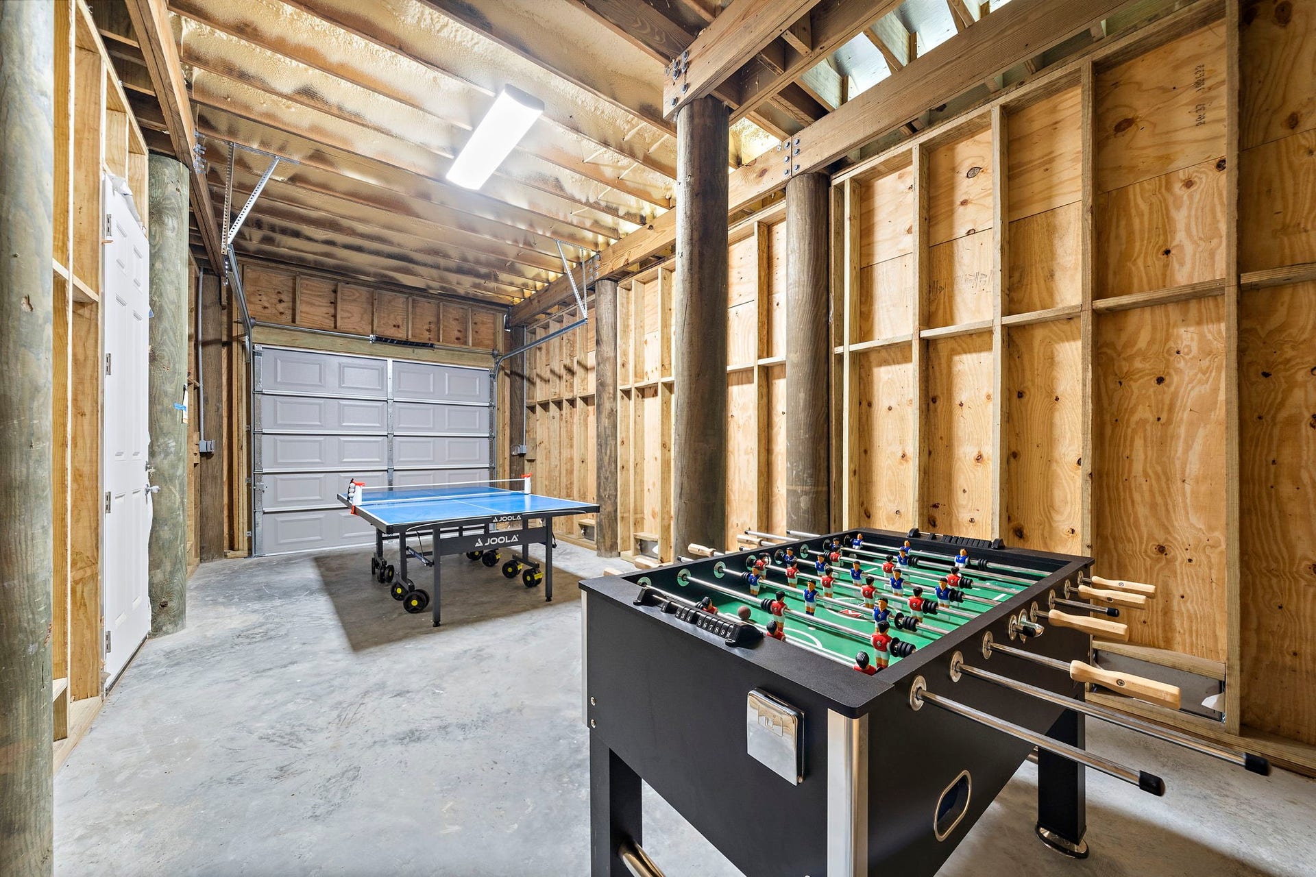 Spacious game room with a foosball table and ping pong setup, featuring rustic wood walls and ample lighting for entertainment.