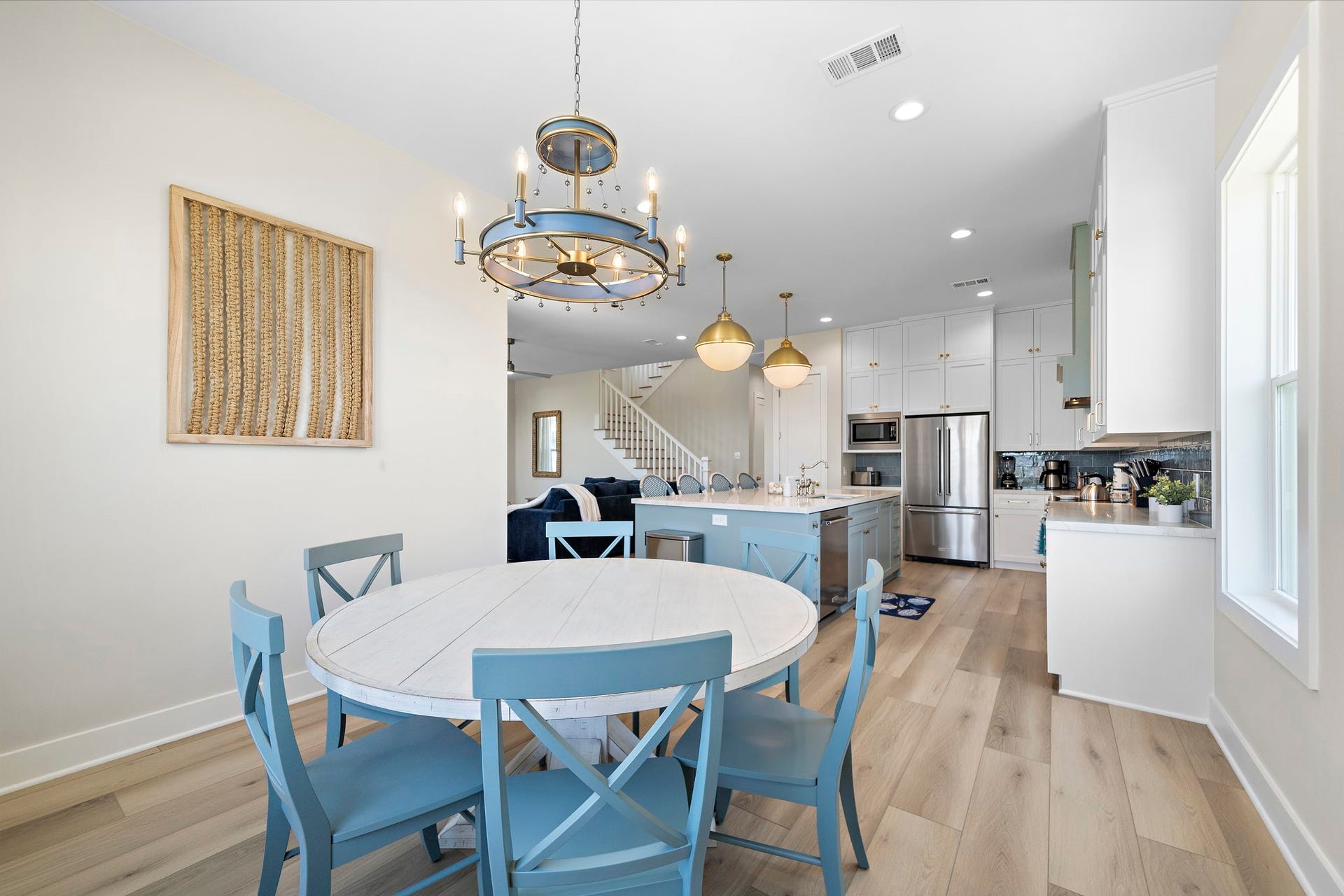 Bright and open dining area with a charming chandelier, adjacent to a modern kitchen featuring an island, stainless steel appliances, and ample cabinetry.