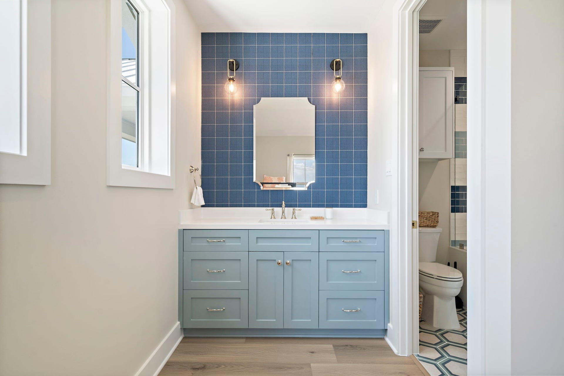 Charming bathroom featuring a stylish blue vanity with ample storage, complemented by a chic blue tile backsplash and modern lighting.