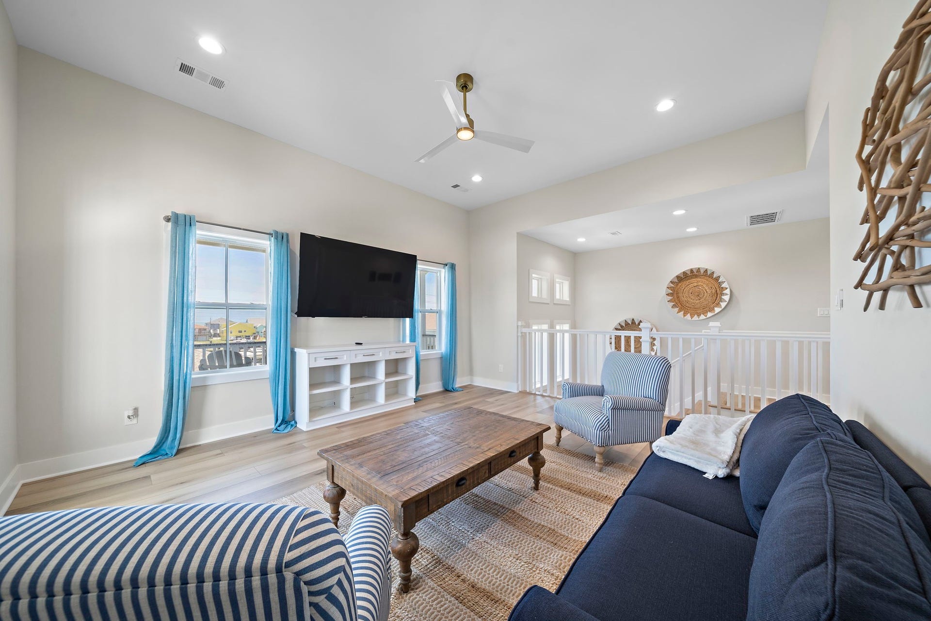Bright and airy living space featuring large windows with coastal views, a ceiling fan, and comfortable seating, perfect for relaxation and entertainment.