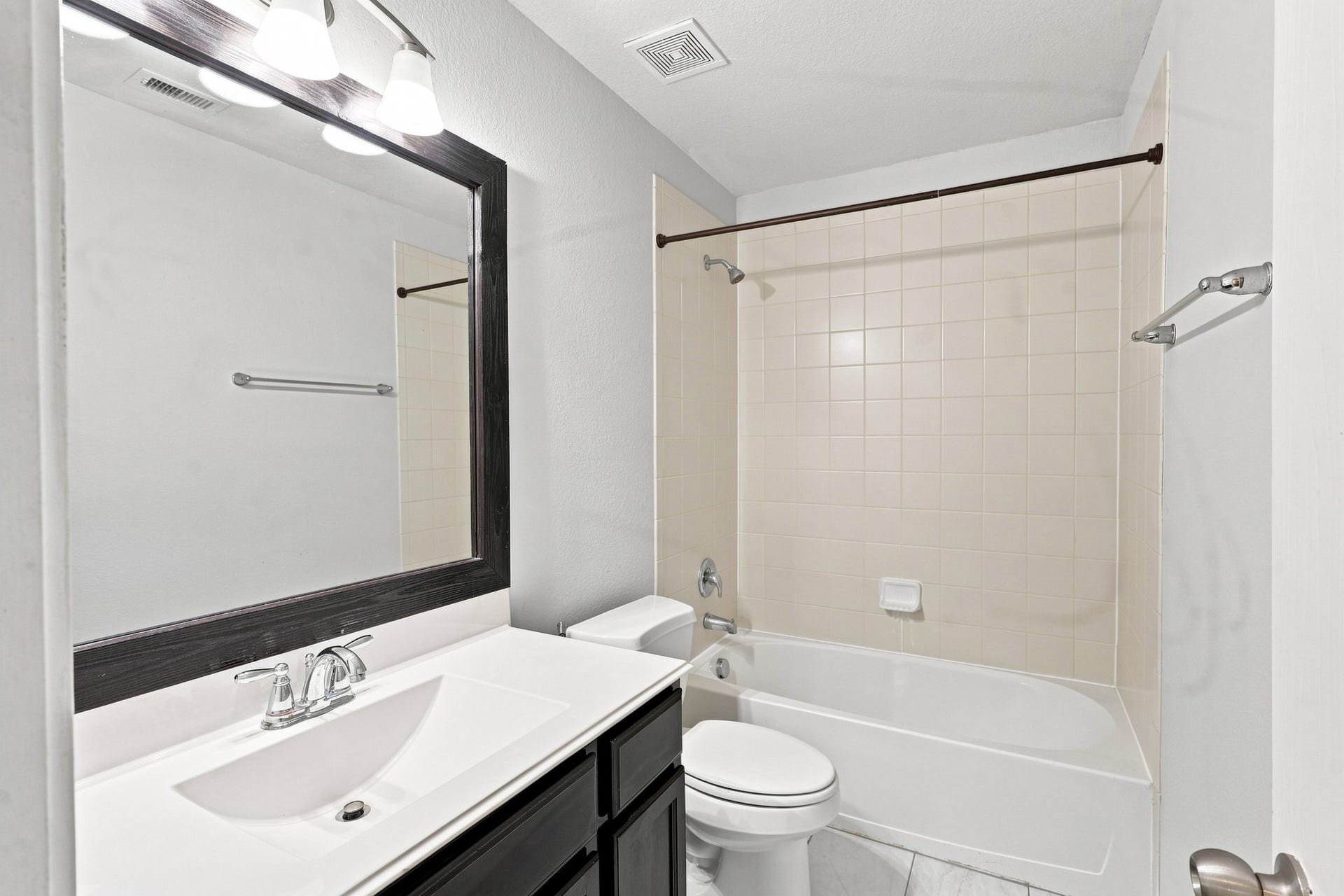 Secondary bathroom with tub/shower combination, large framed mirror, and dark cabinetry.