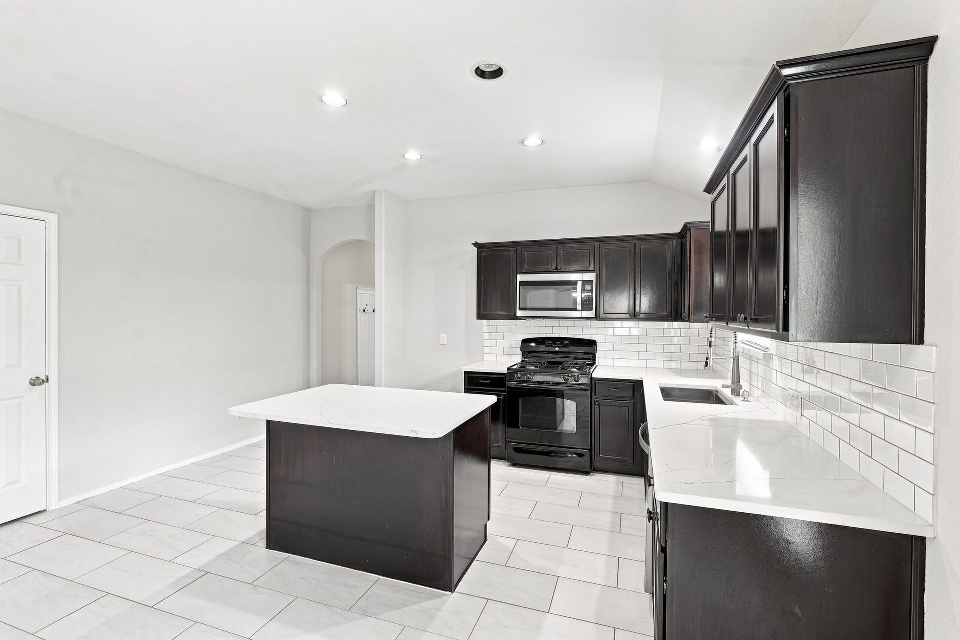 Kitchen featuring dark cabinetry, white countertops, subway tile backsplash, stainless steel appliances, and center island.