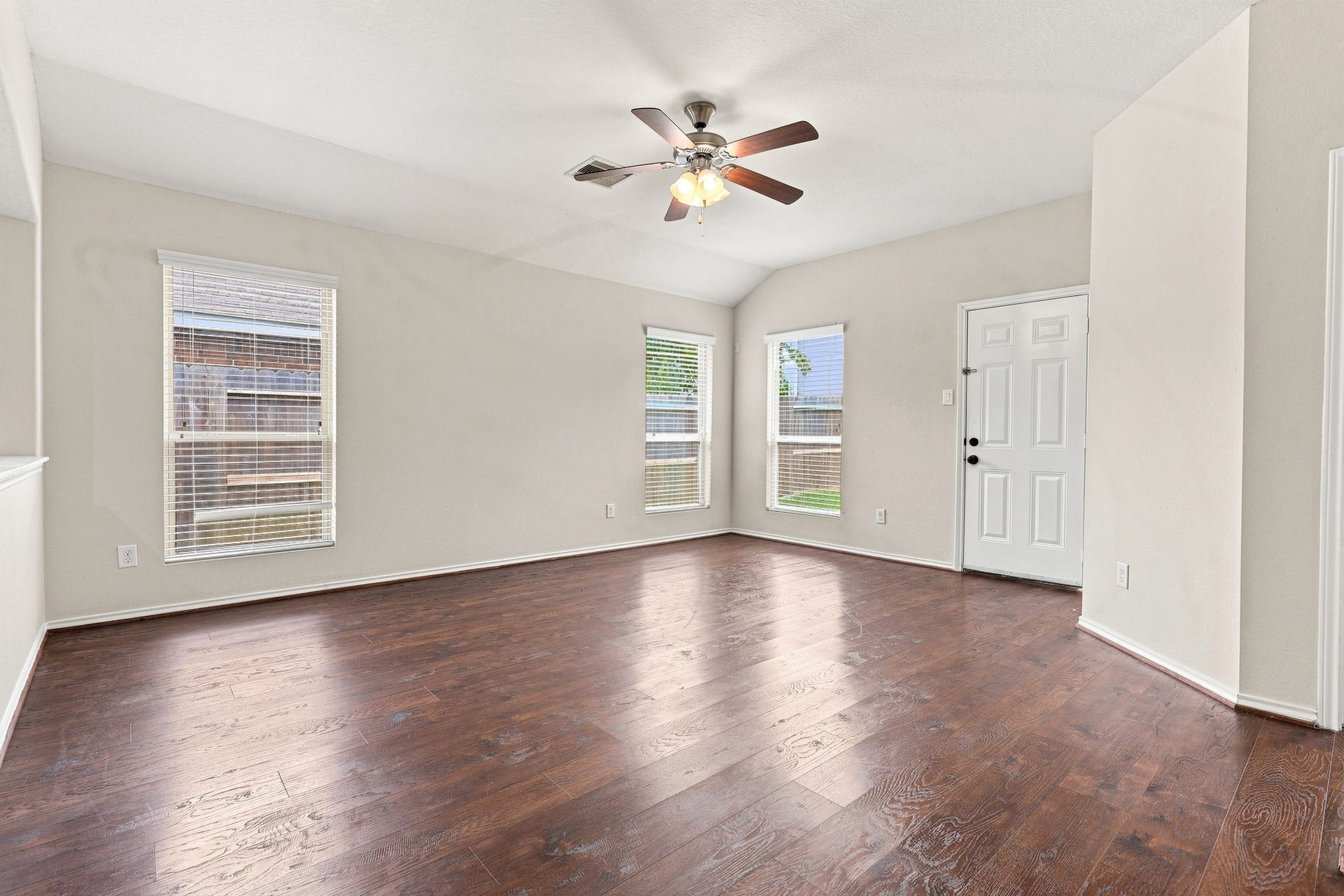 Generously sized living room with upgraded flooring, high ceiling, ceiling fan, and abundant natural light.