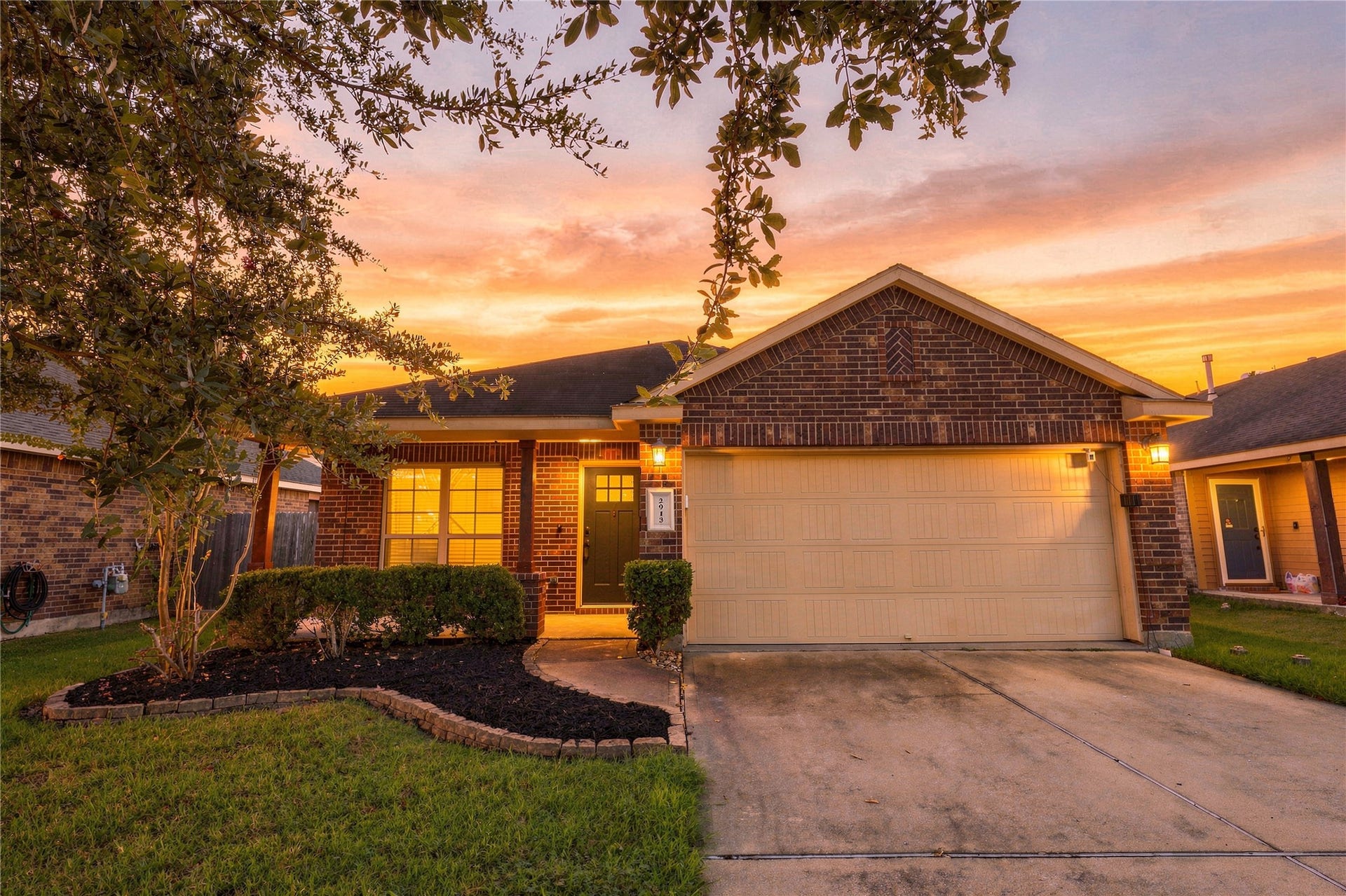 Twilight exterior showcasing the homes brick elevation, mature landscaping, and 2-car garage.