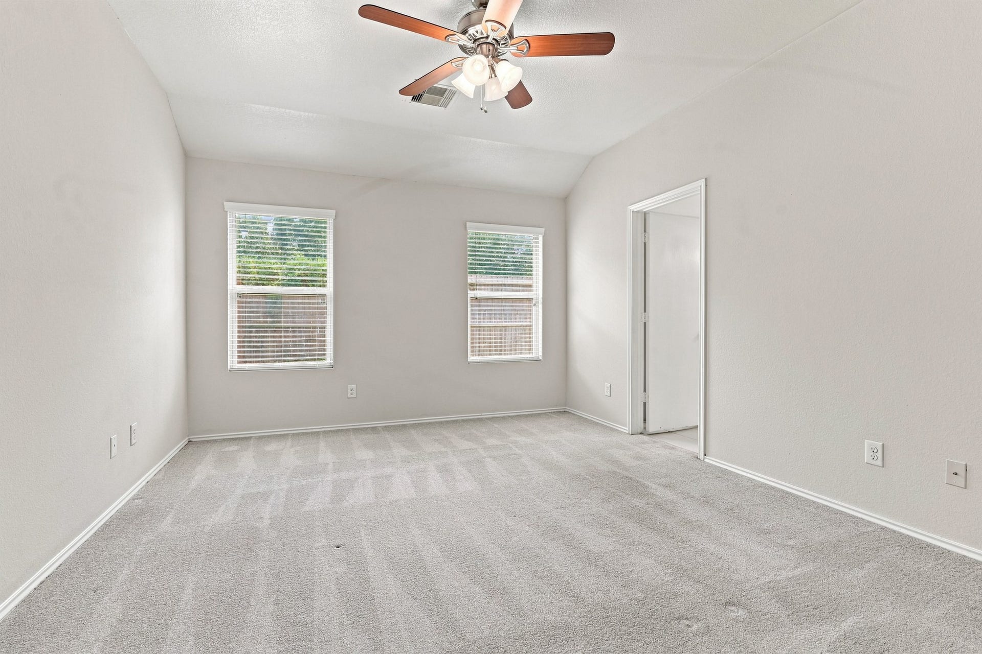 Spacious primary bedroom with vaulted ceiling, ceiling fan, neutral carpet, and multiple windows.