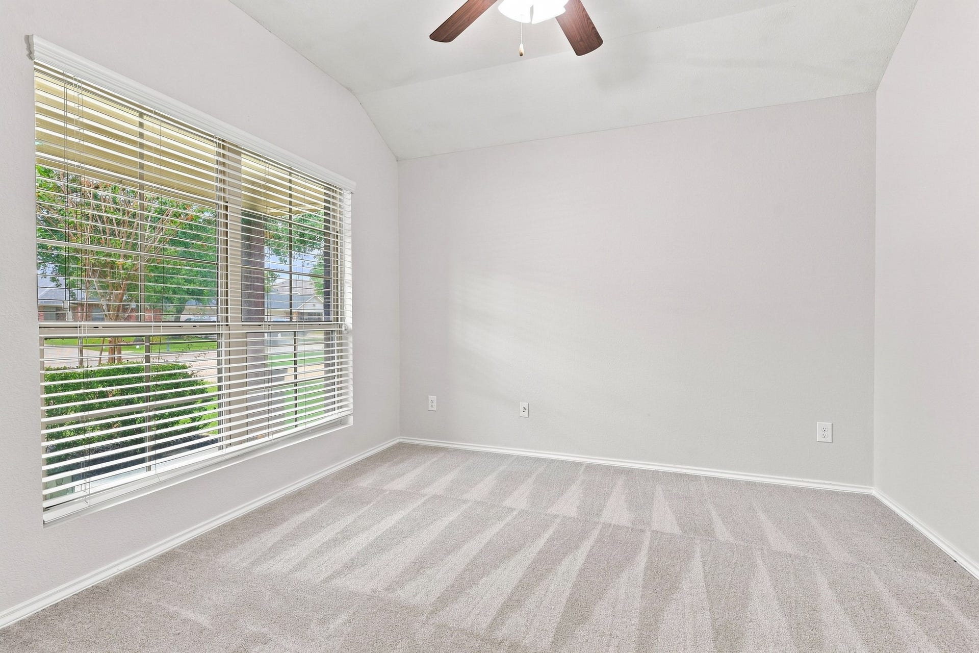 Dedicated study/home office with vaulted ceiling, ceiling fan, large window, and neutral carpet.