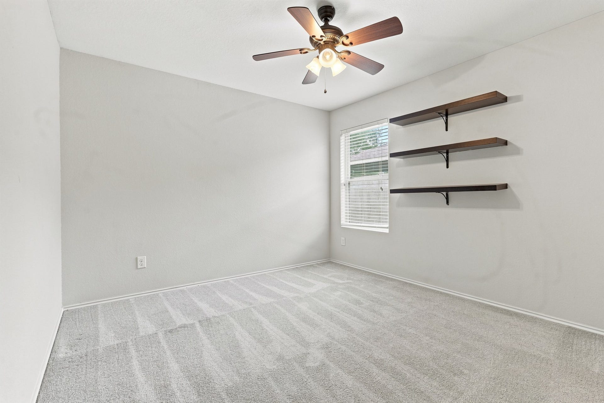 Second bedroom with ceiling fan, window, and floating wall shelves