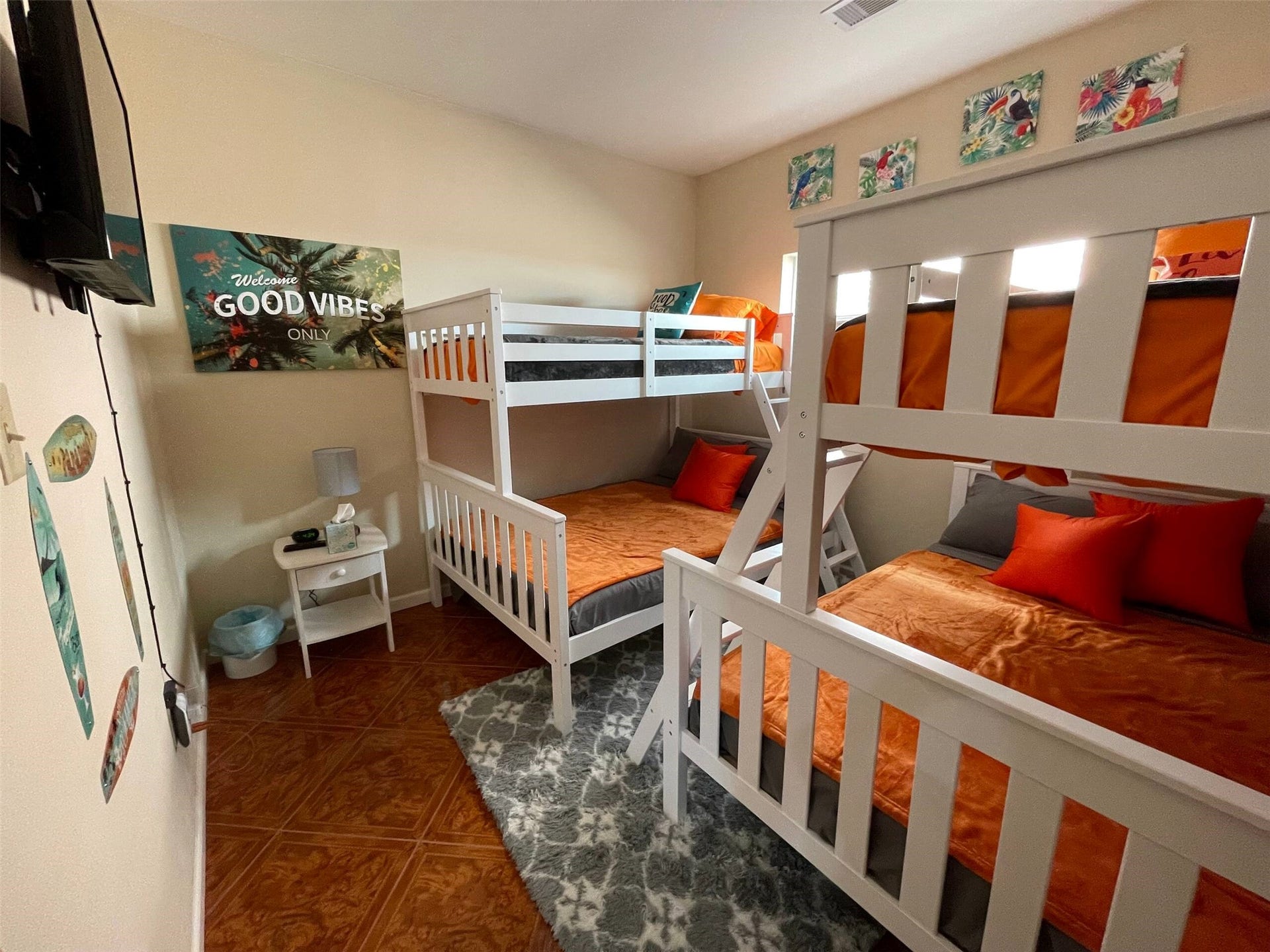 Bright and inviting bedroom featuring two sets of white bunk beds with vibrant orange bedding, complemented by playful wall art and a cozy area rug. Perfect for maximizing space and comfort.