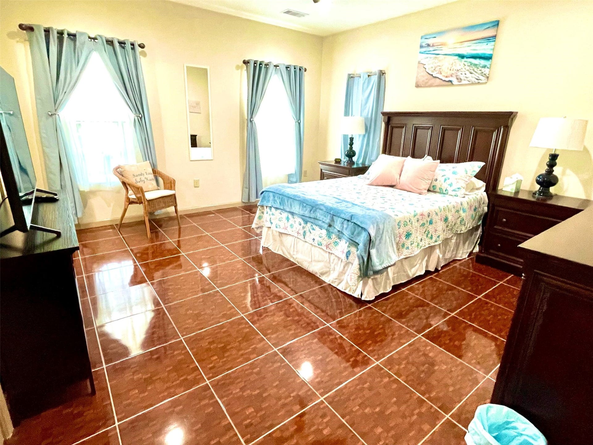 Spacious bedroom with glossy tile floors, elegant dark wood furniture, and soft blue accents, creating a serene and inviting atmosphere.