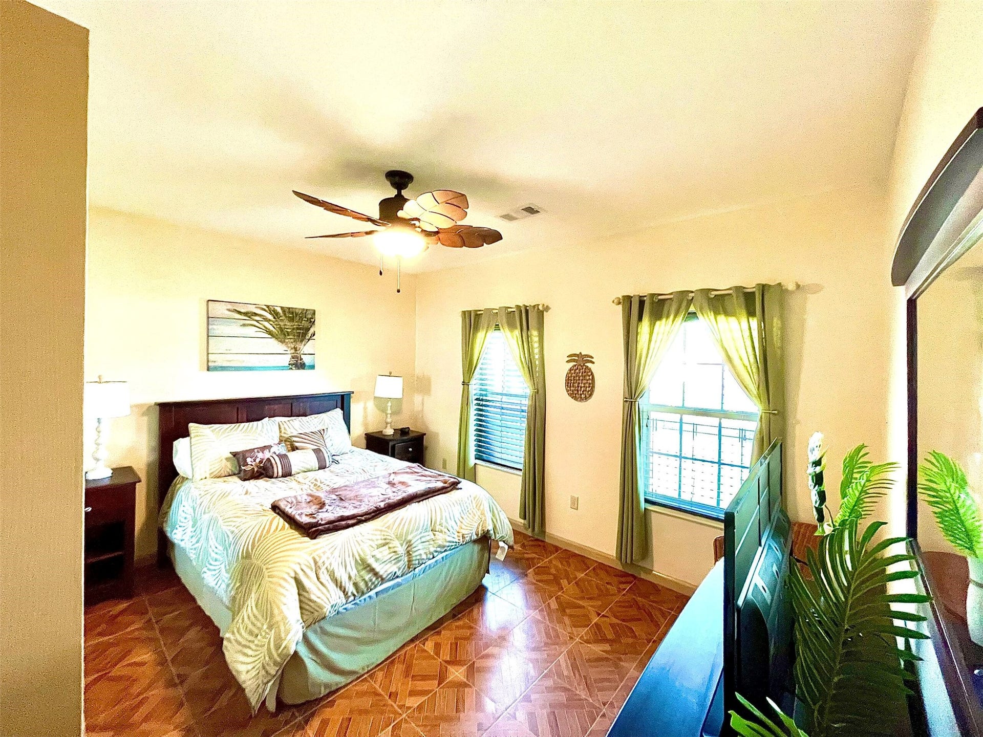 Cozy bedroom with natural light, featuring a stylish ceiling fan, warm wooden flooring, and vibrant decor for a welcoming atmosphere.